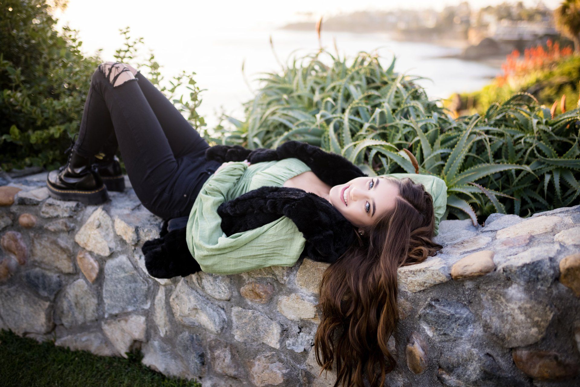 A woman is laying on a stone wall next to a body of water.