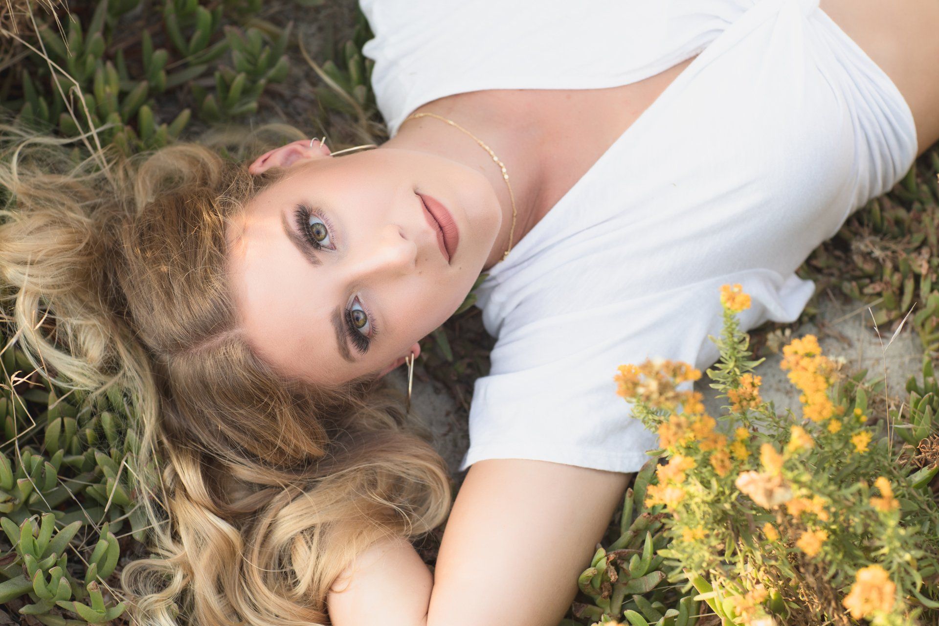 A woman in a white shirt is laying in the grass next to flowers.