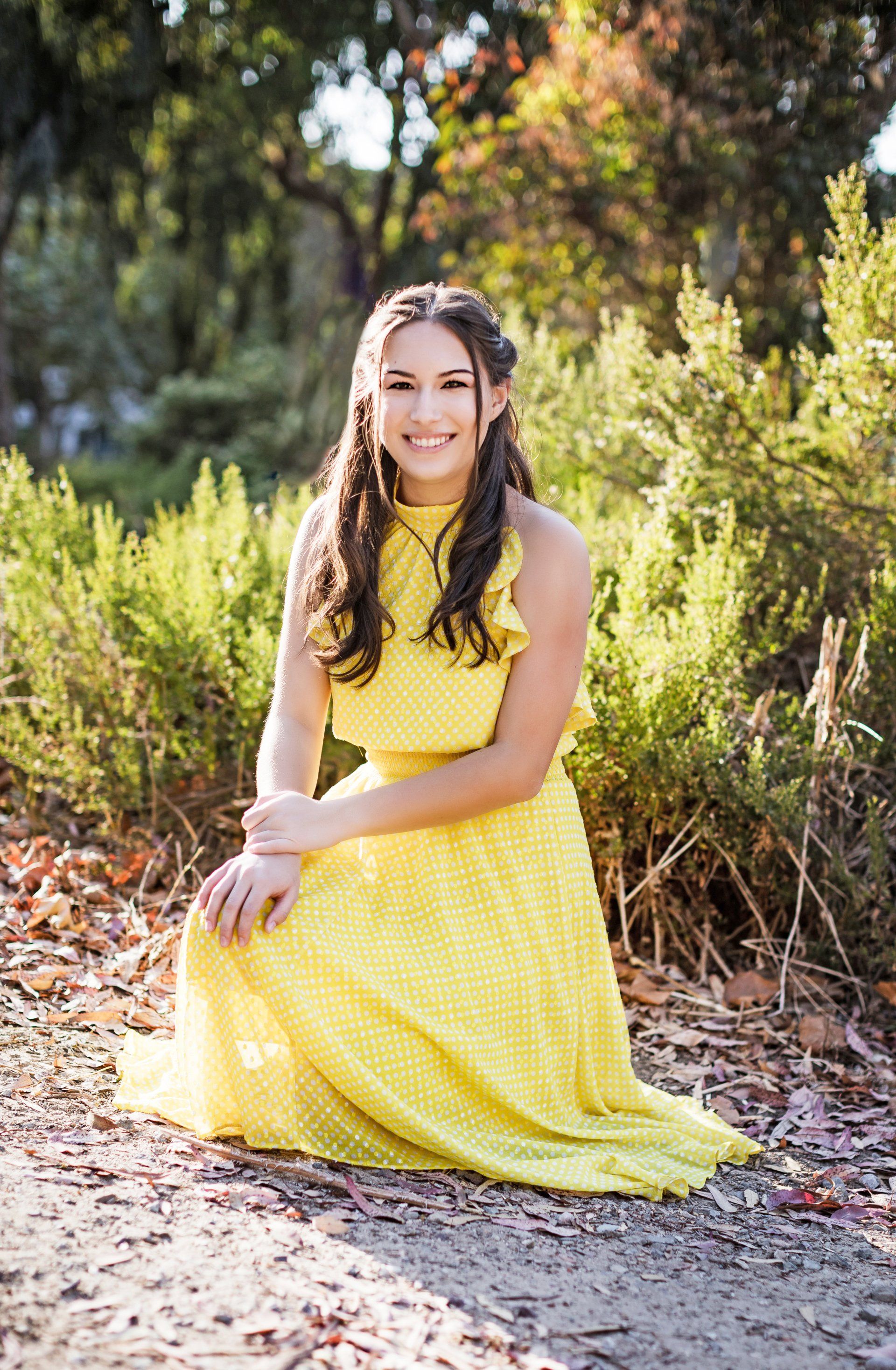 A woman in a yellow dress is kneeling down in the dirt.