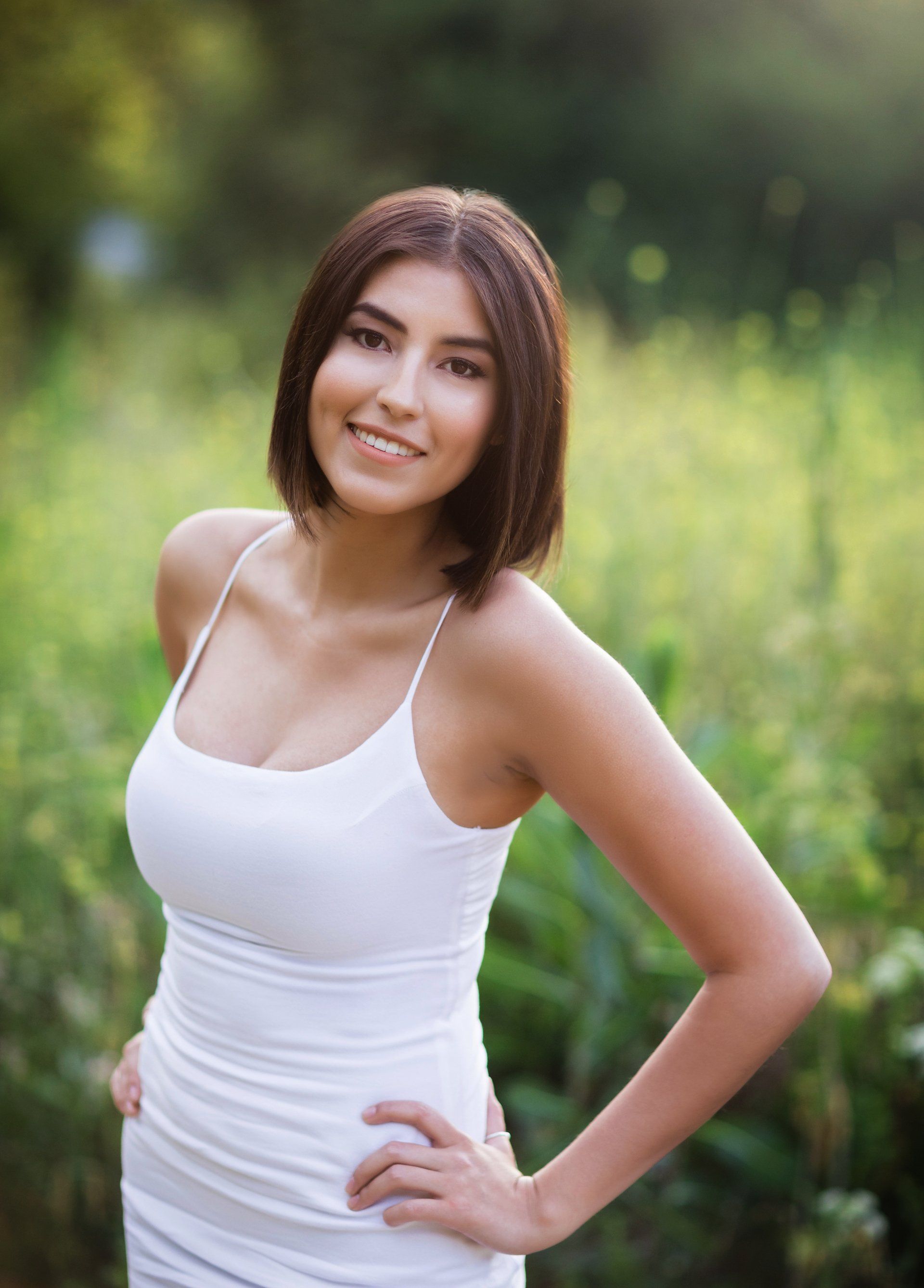 A woman in a white dress is standing in a field with her hands on her hips.