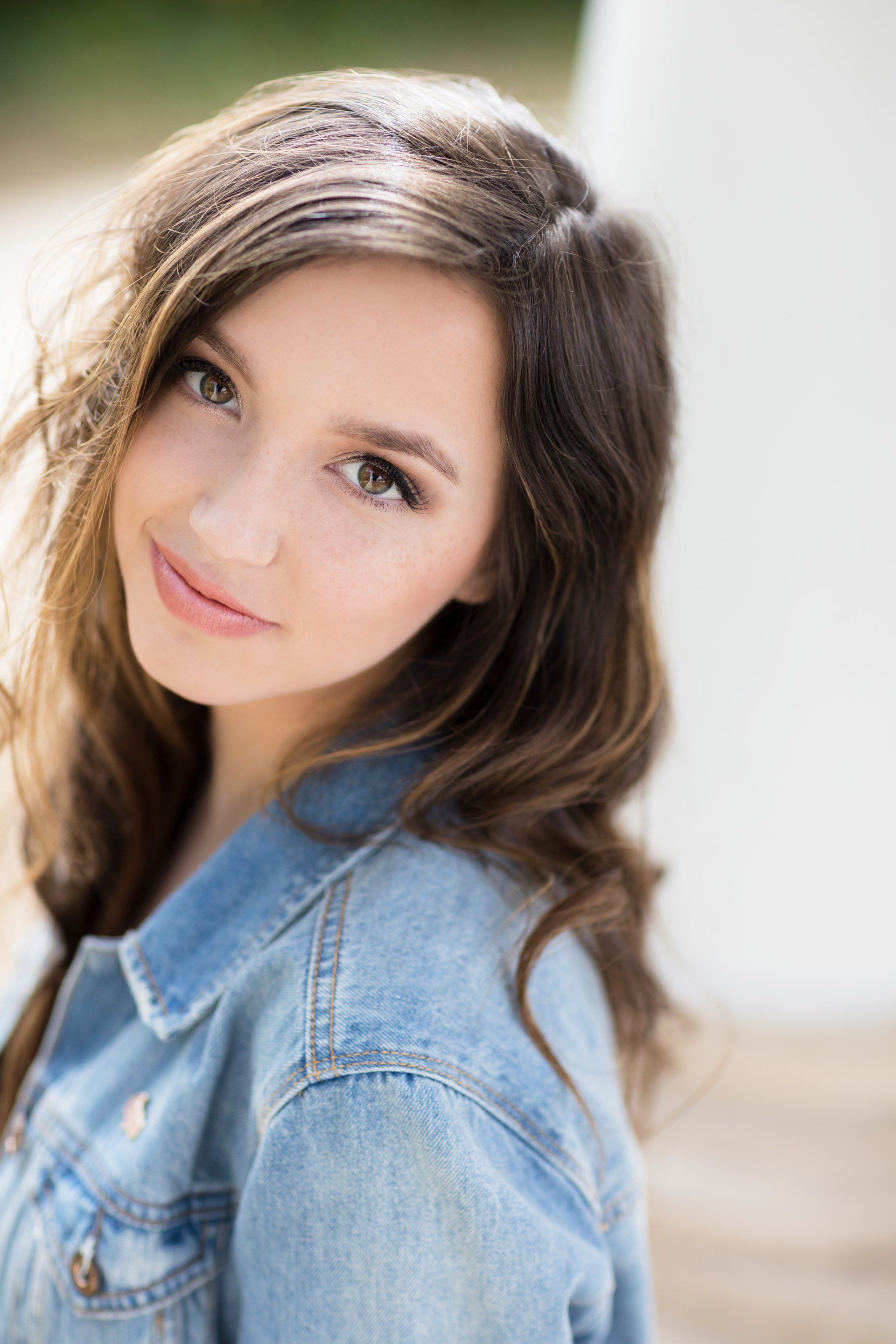 A young woman wearing a denim jacket is looking at the camera.