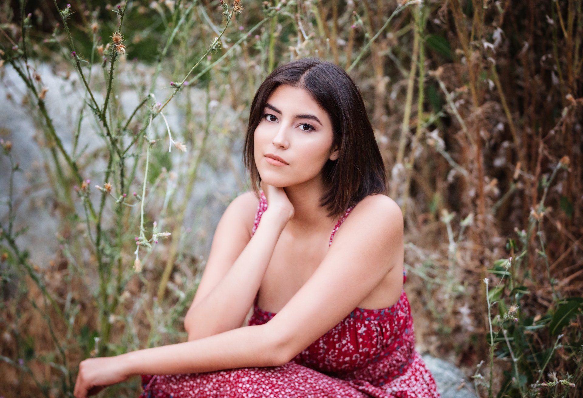 A woman in a red dress is sitting in the grass.