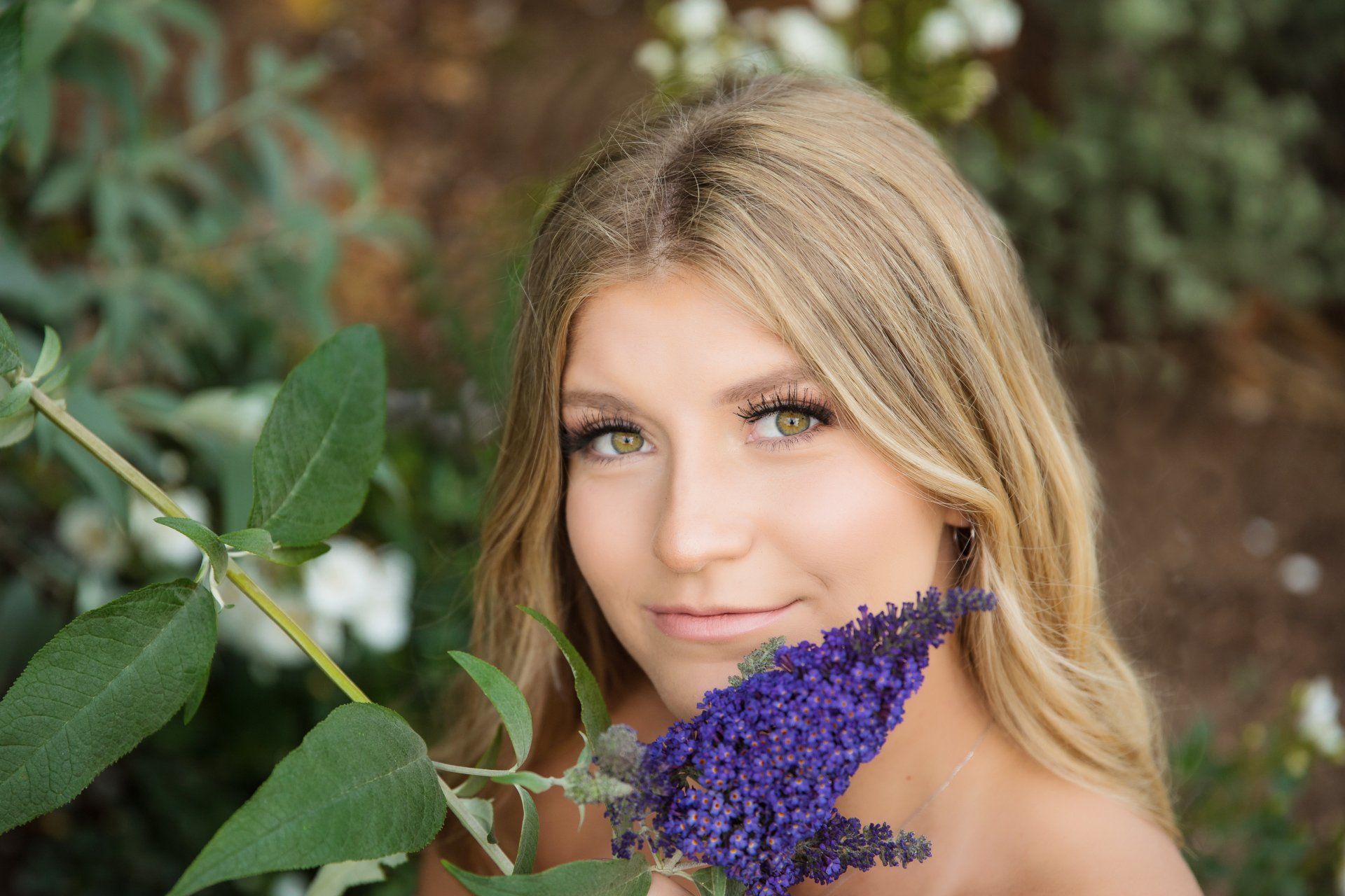 A young woman is holding a purple flower in front of her face.