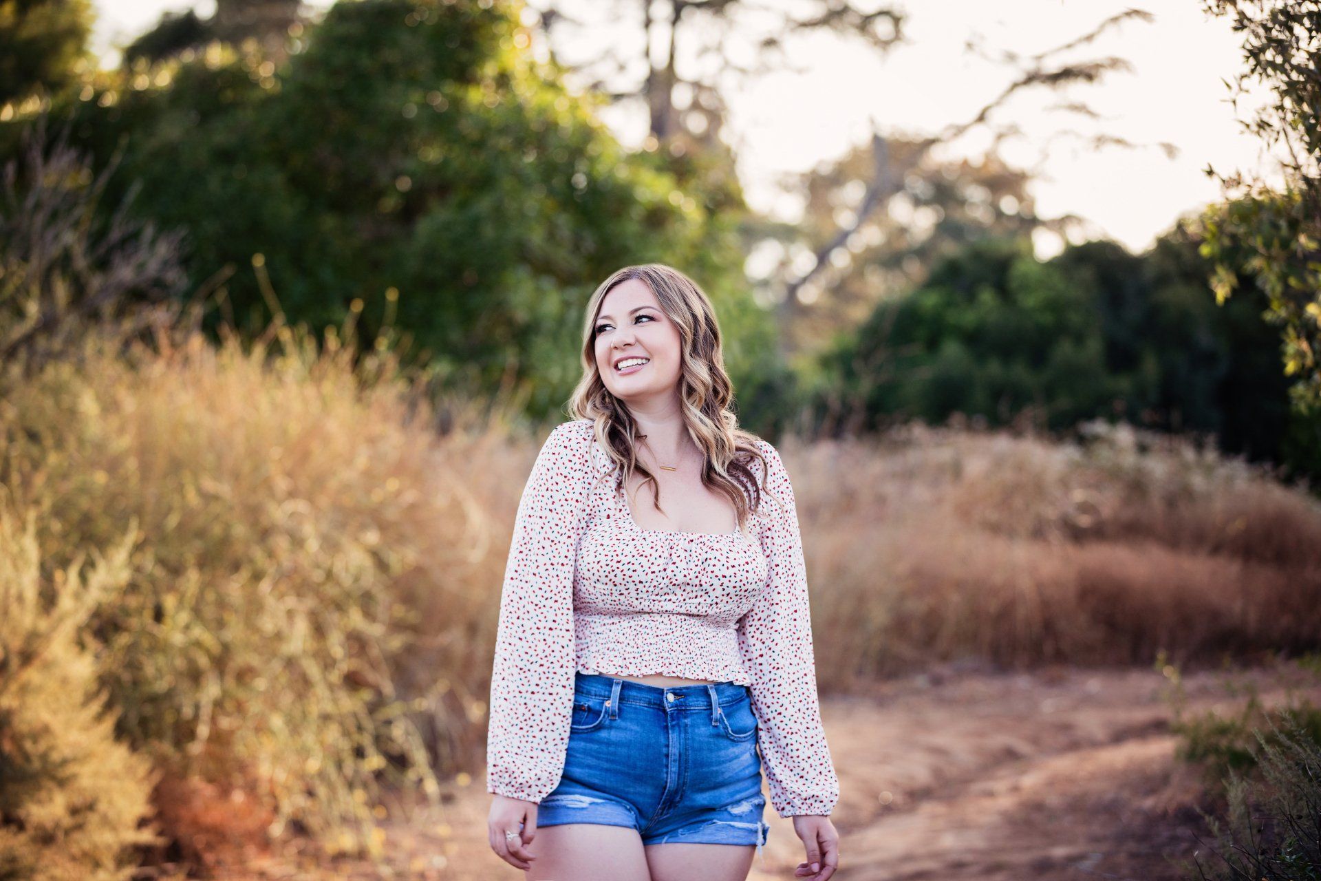 A woman is walking down a dirt road in a field.