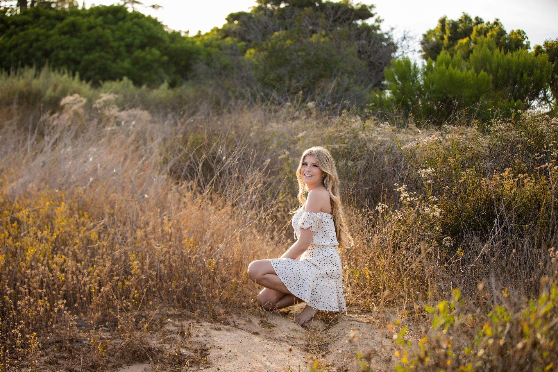 A woman in a white dress is kneeling down in a field.