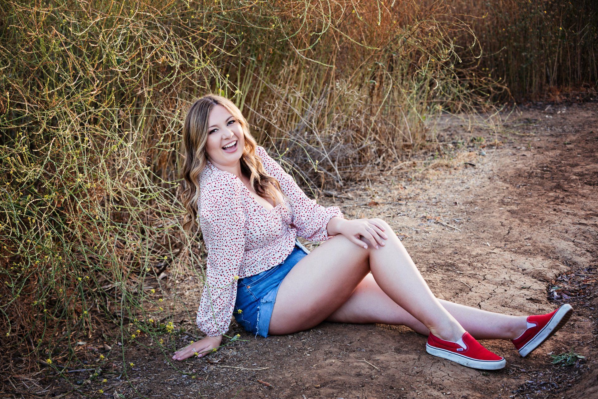 A woman is sitting on the ground in a field with her legs crossed.