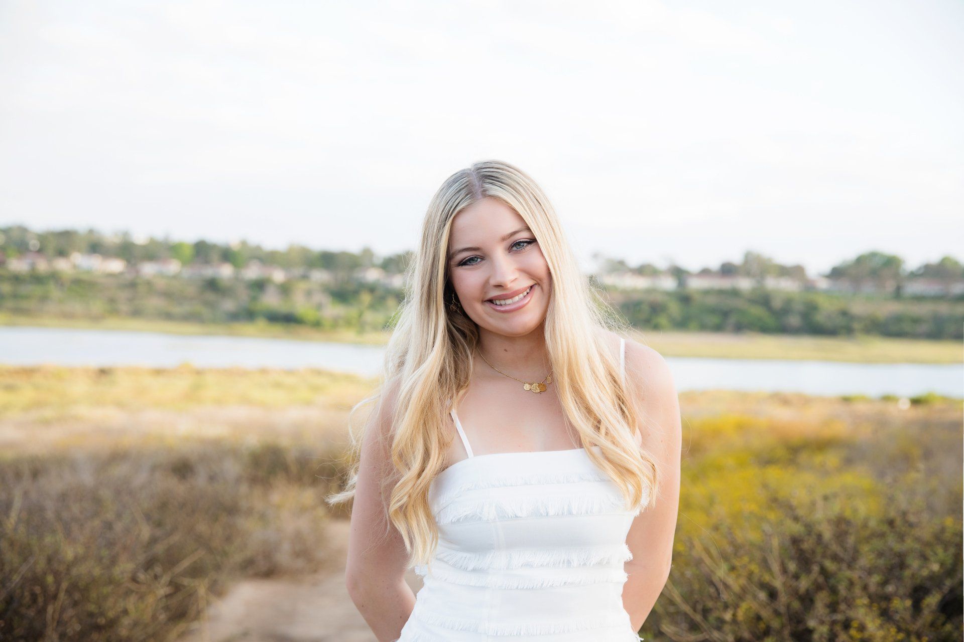 A young woman in a white dress is standing in a field.