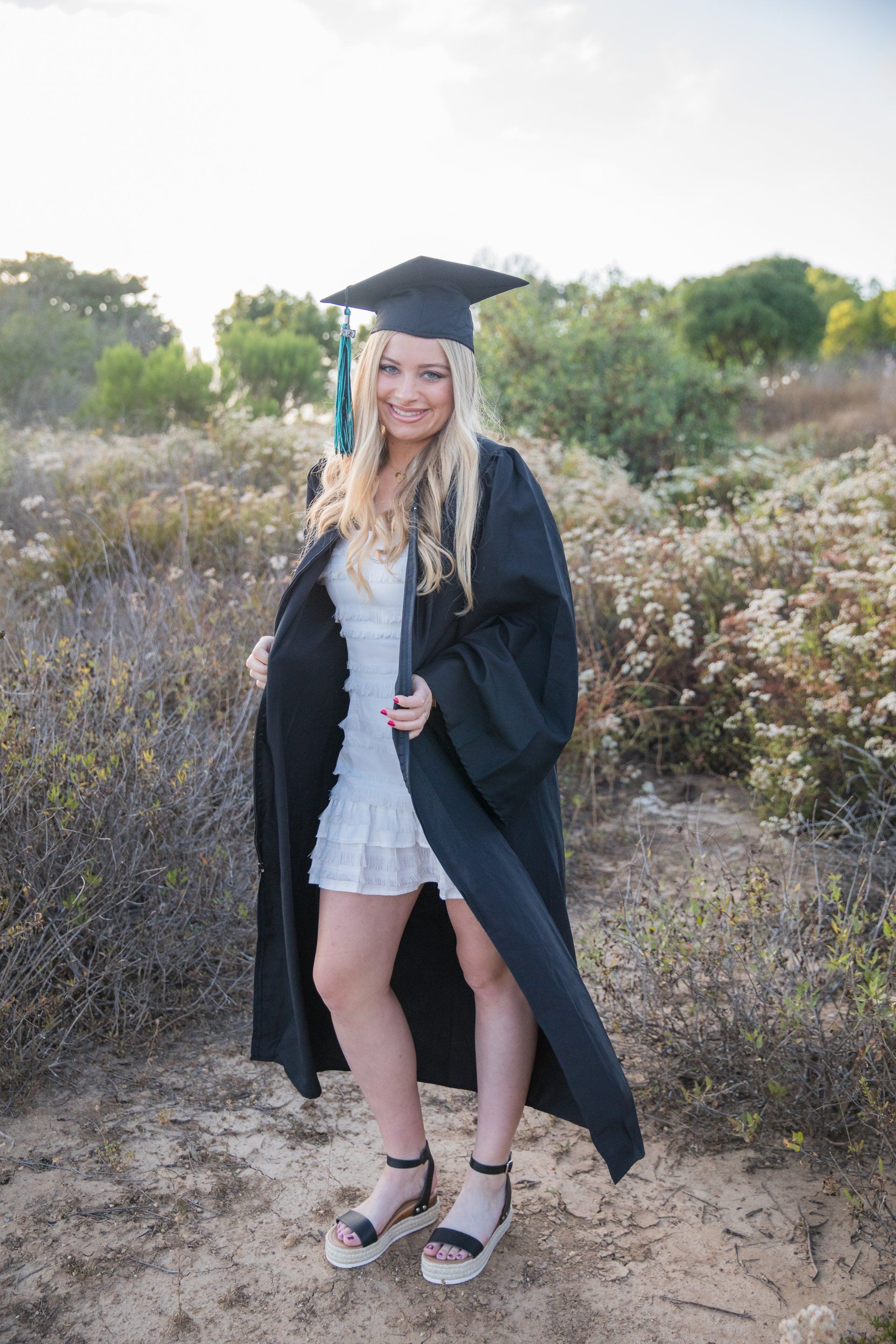 A woman in a graduation cap and gown is standing in a field.