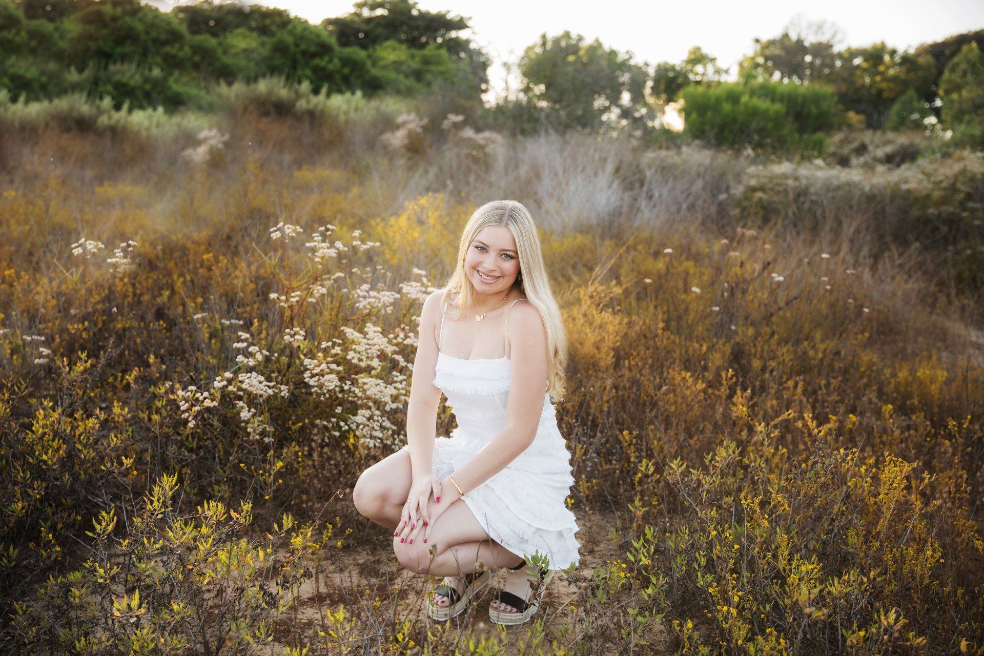 A woman in a white dress is kneeling in a field of flowers.