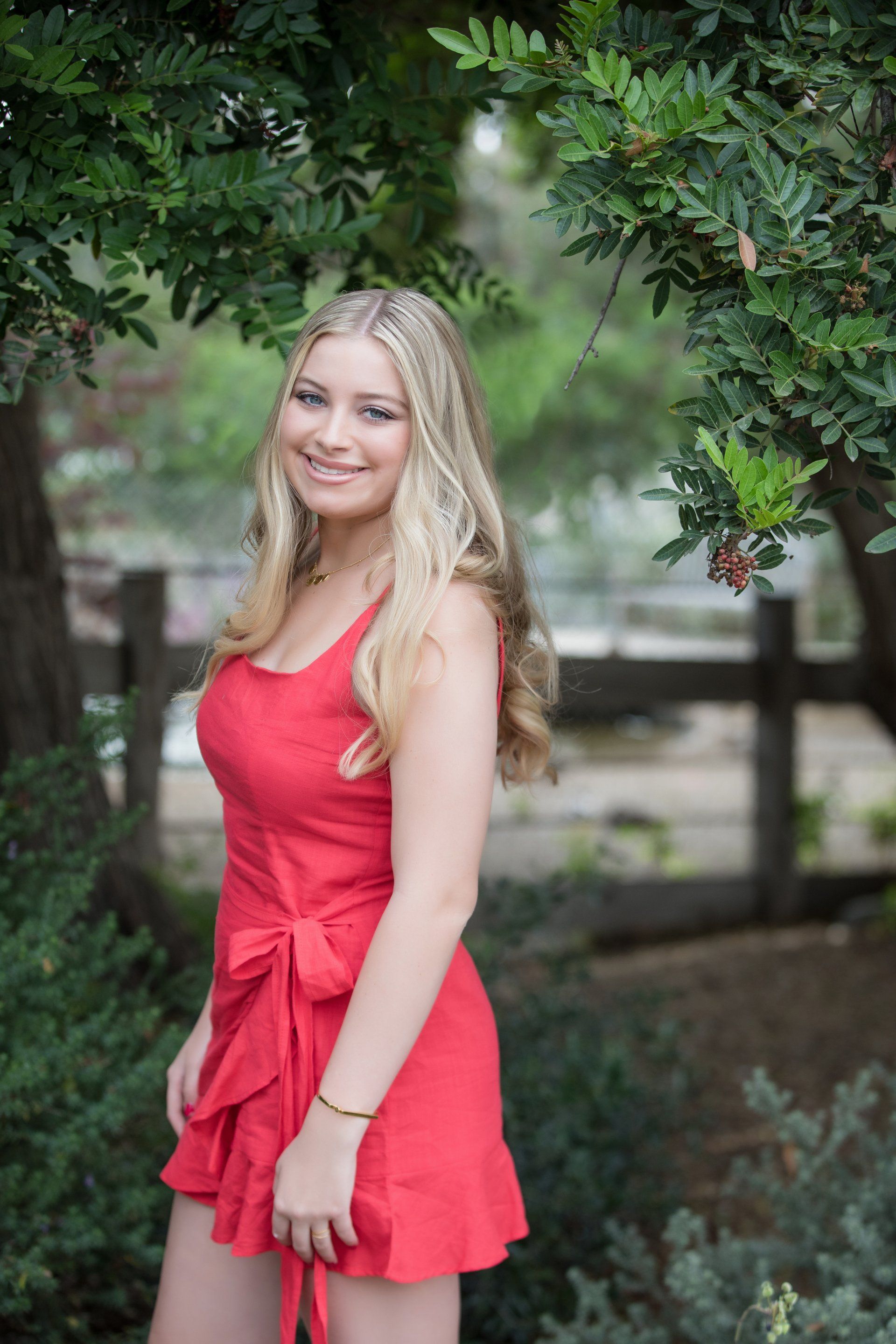 A woman in a red dress is standing in front of a tree.