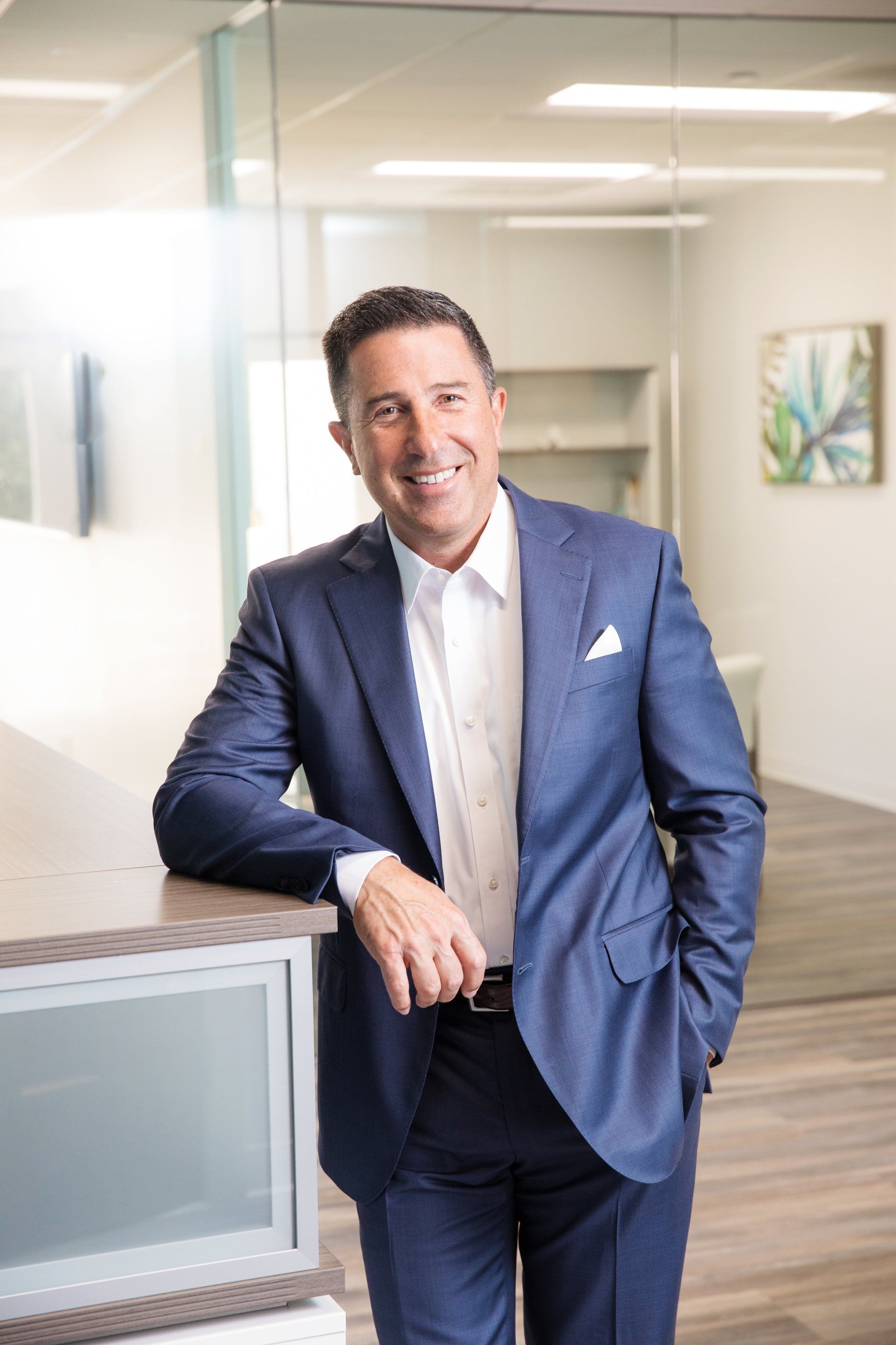A man in a suit is leaning on a counter in an office.