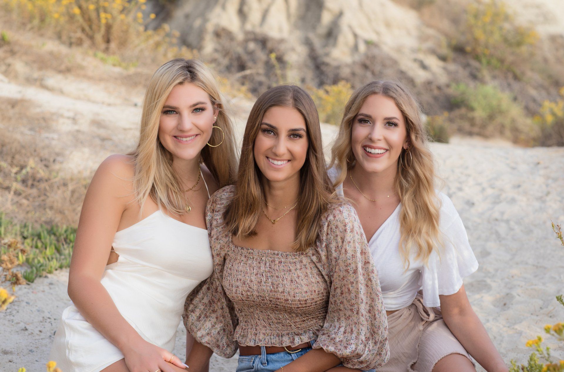 Three young women are posing for a picture on the beach.