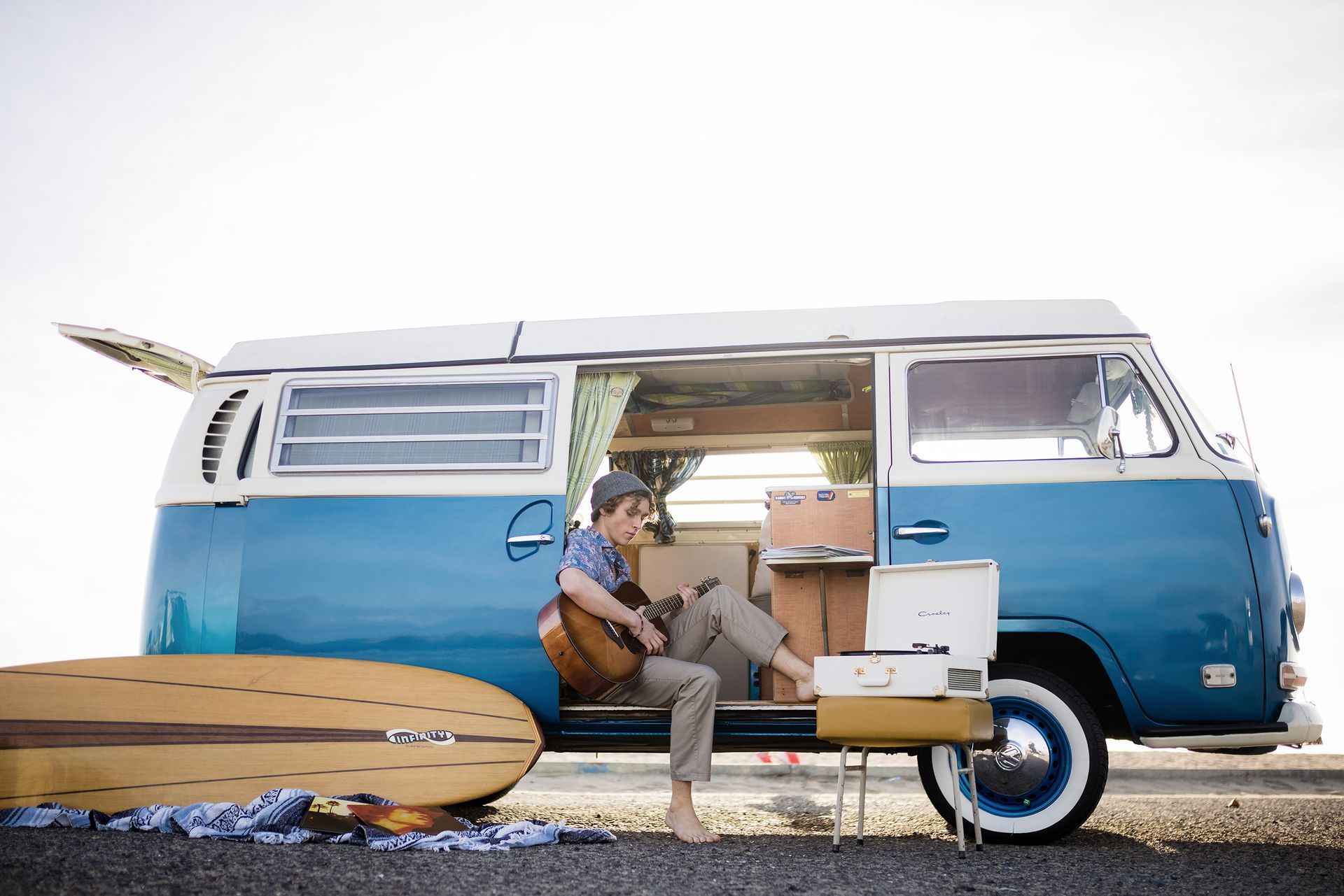 A man is sitting in a blue van playing a guitar.
