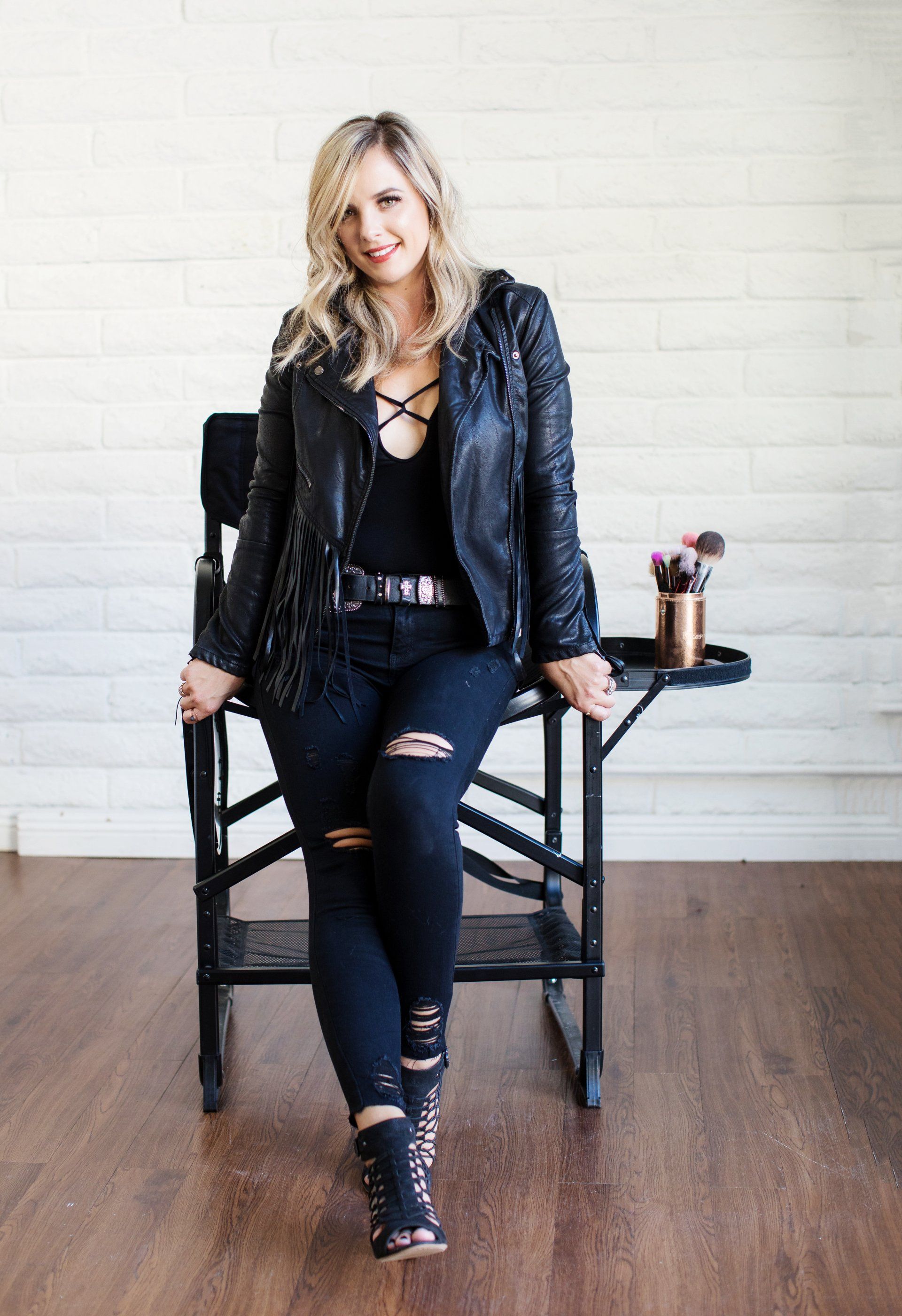 A woman in a leather jacket is sitting on a makeup chair.