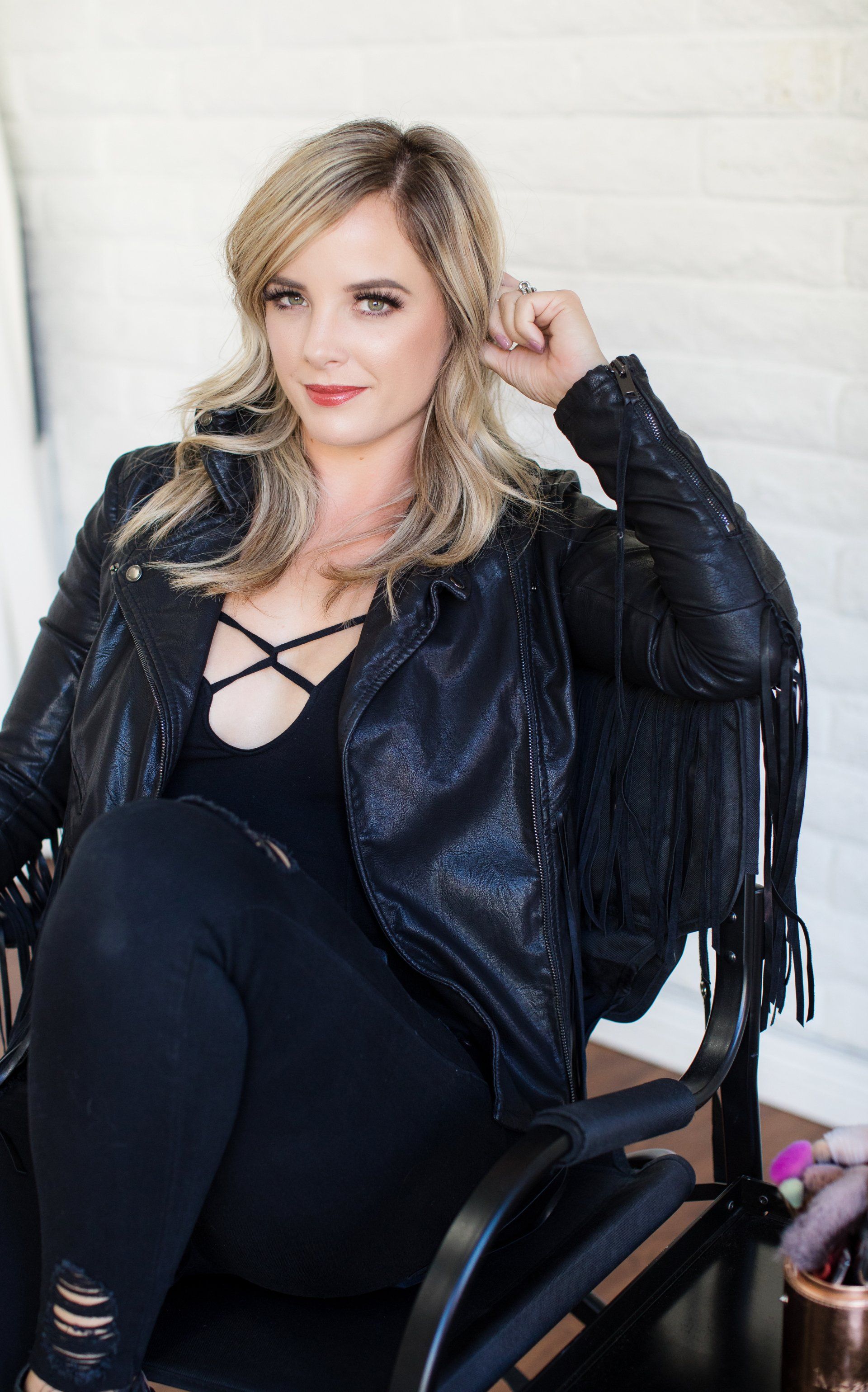 A woman in a black leather jacket is sitting in a chair.