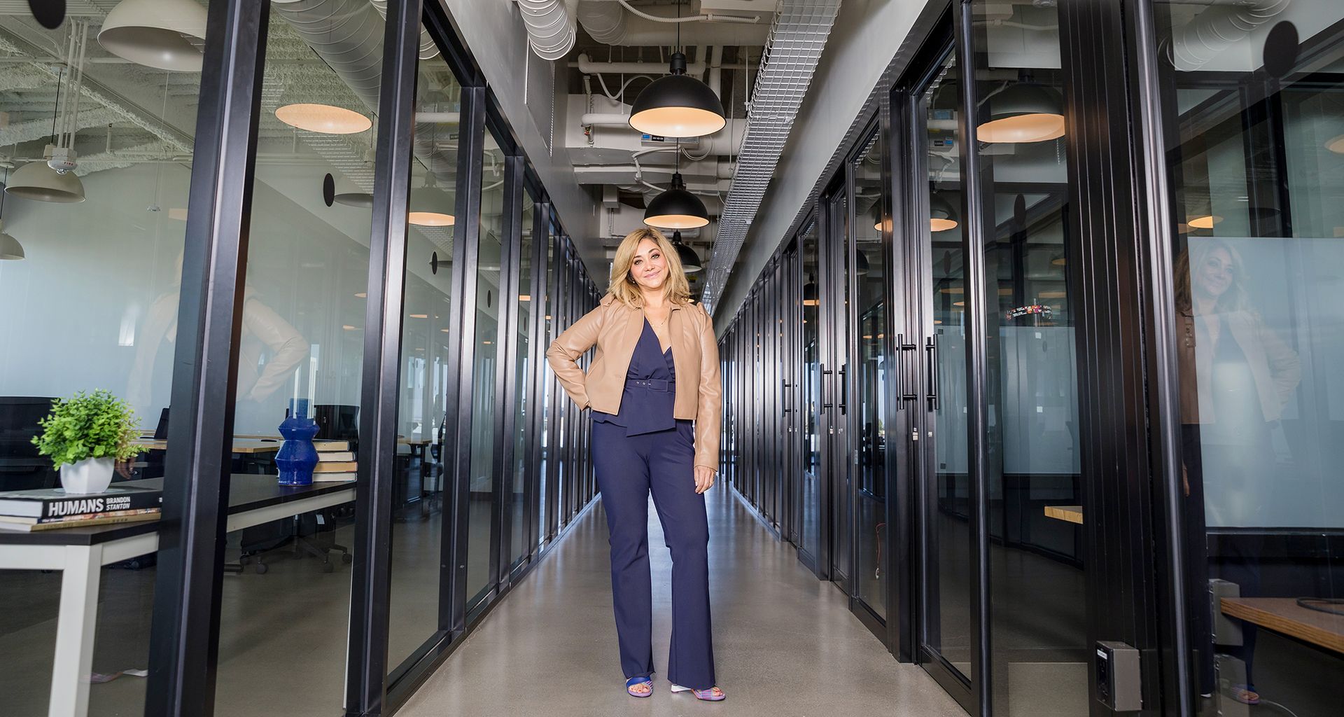 A woman is standing in a long hallway in an office building.