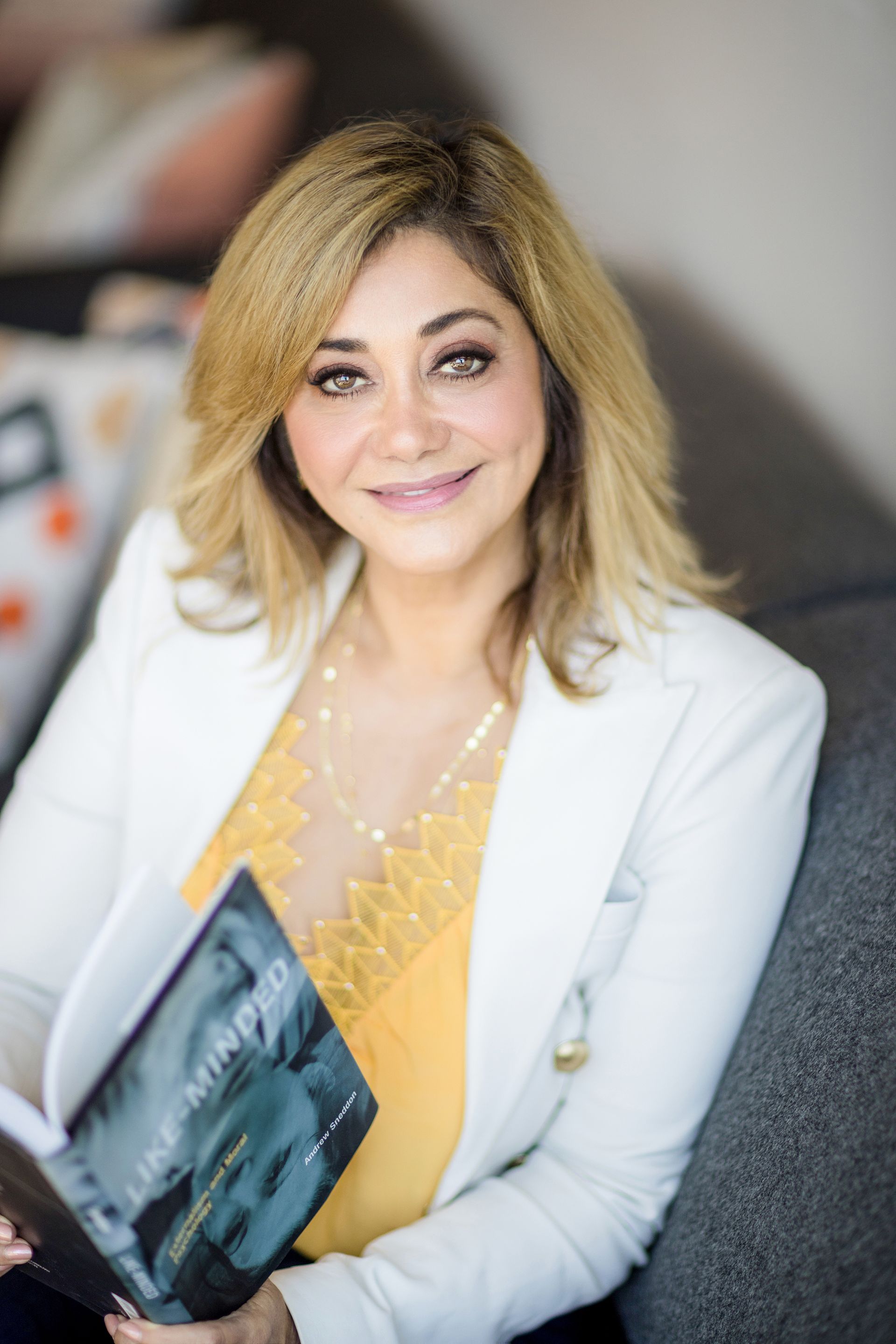 A woman is sitting on a couch holding a book.