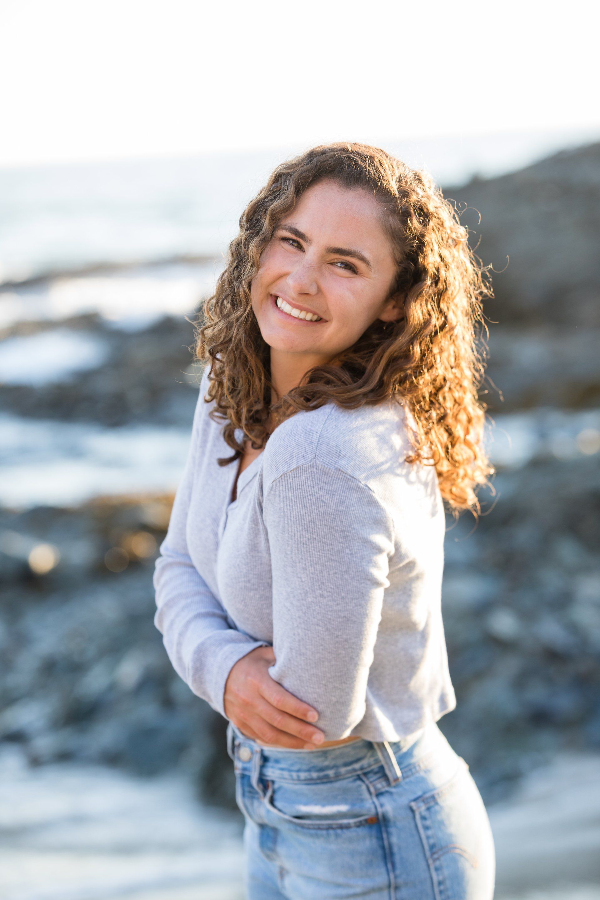 A woman is standing on a beach with her arms crossed and smiling.