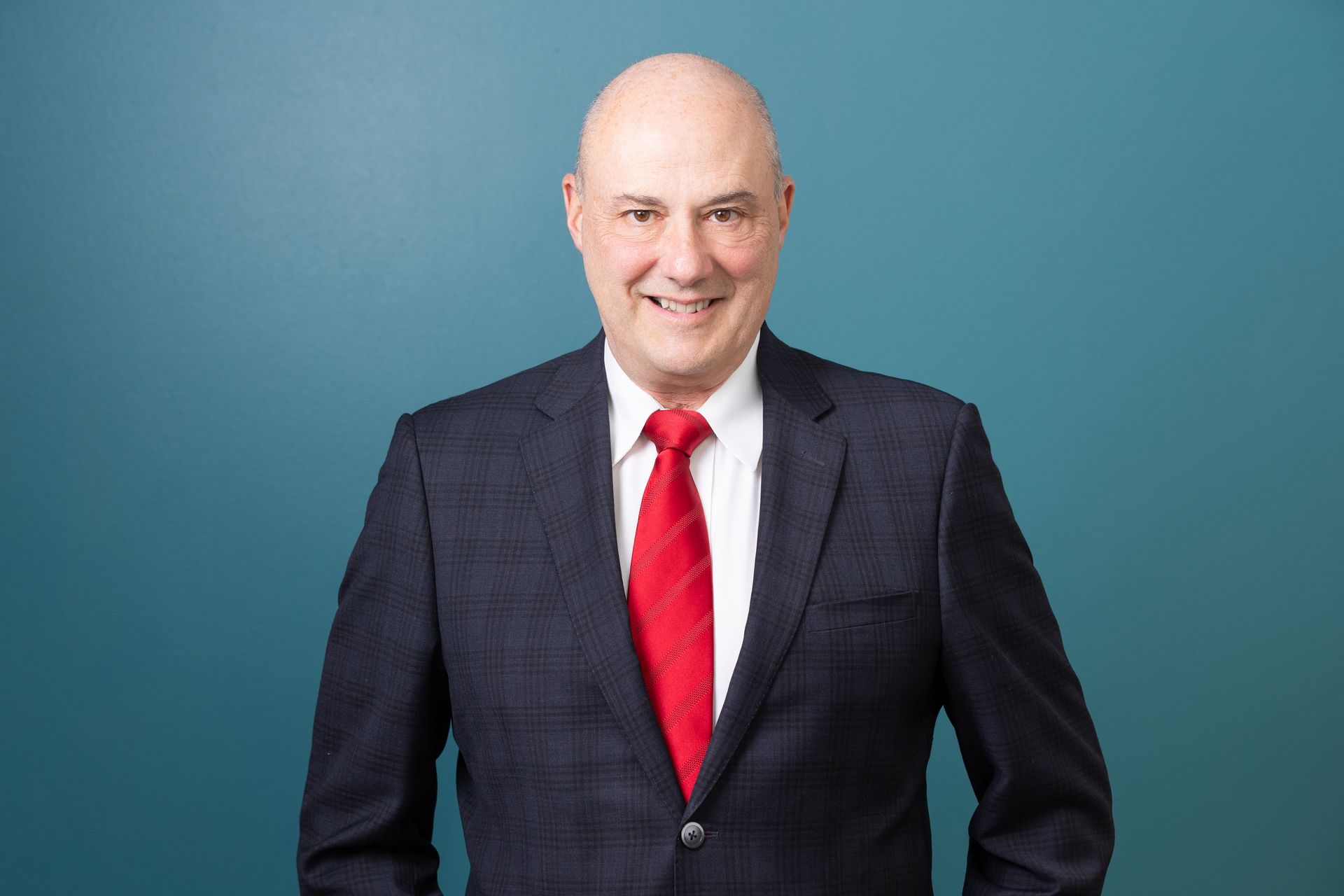 A man in a suit and red tie is standing in front of a blue wall.
