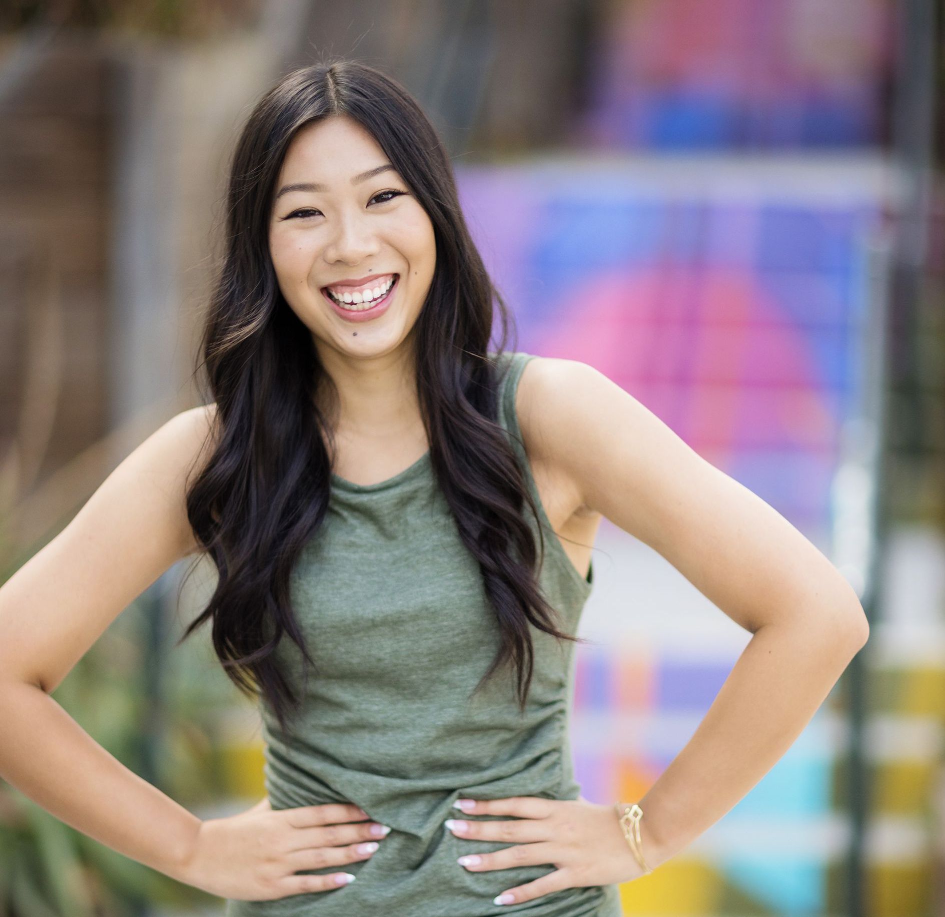 A woman in a green tank top is smiling with her hands on her hips.