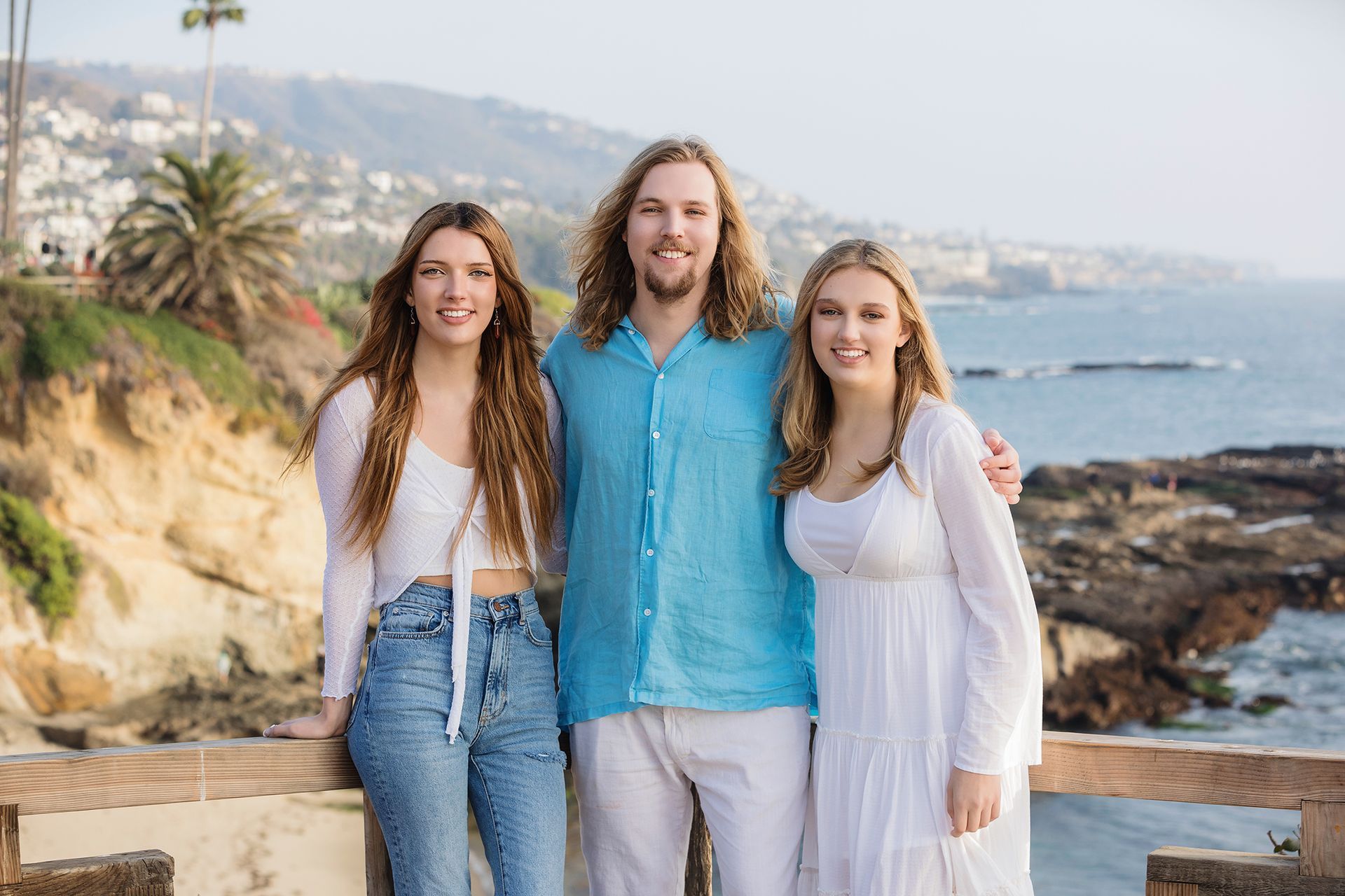 A man and two women are posing for a picture on a bridge overlooking the ocean.