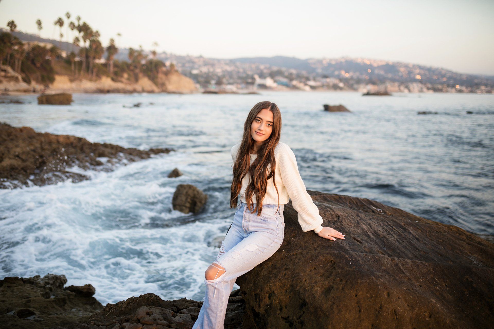 A woman is sitting on a rock near the ocean.