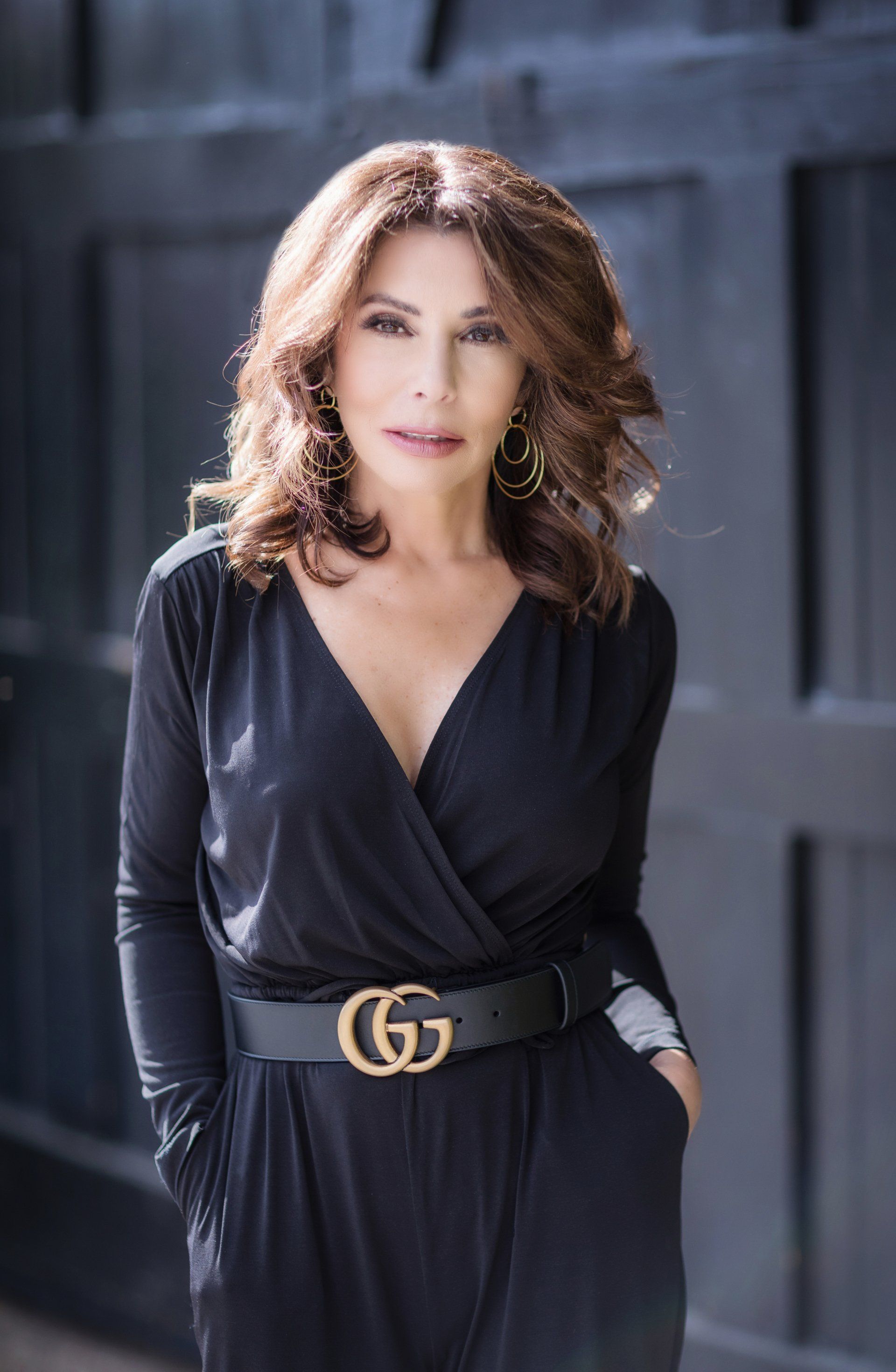 A woman in a black jumpsuit with a gucci belt is standing in front of a black door.