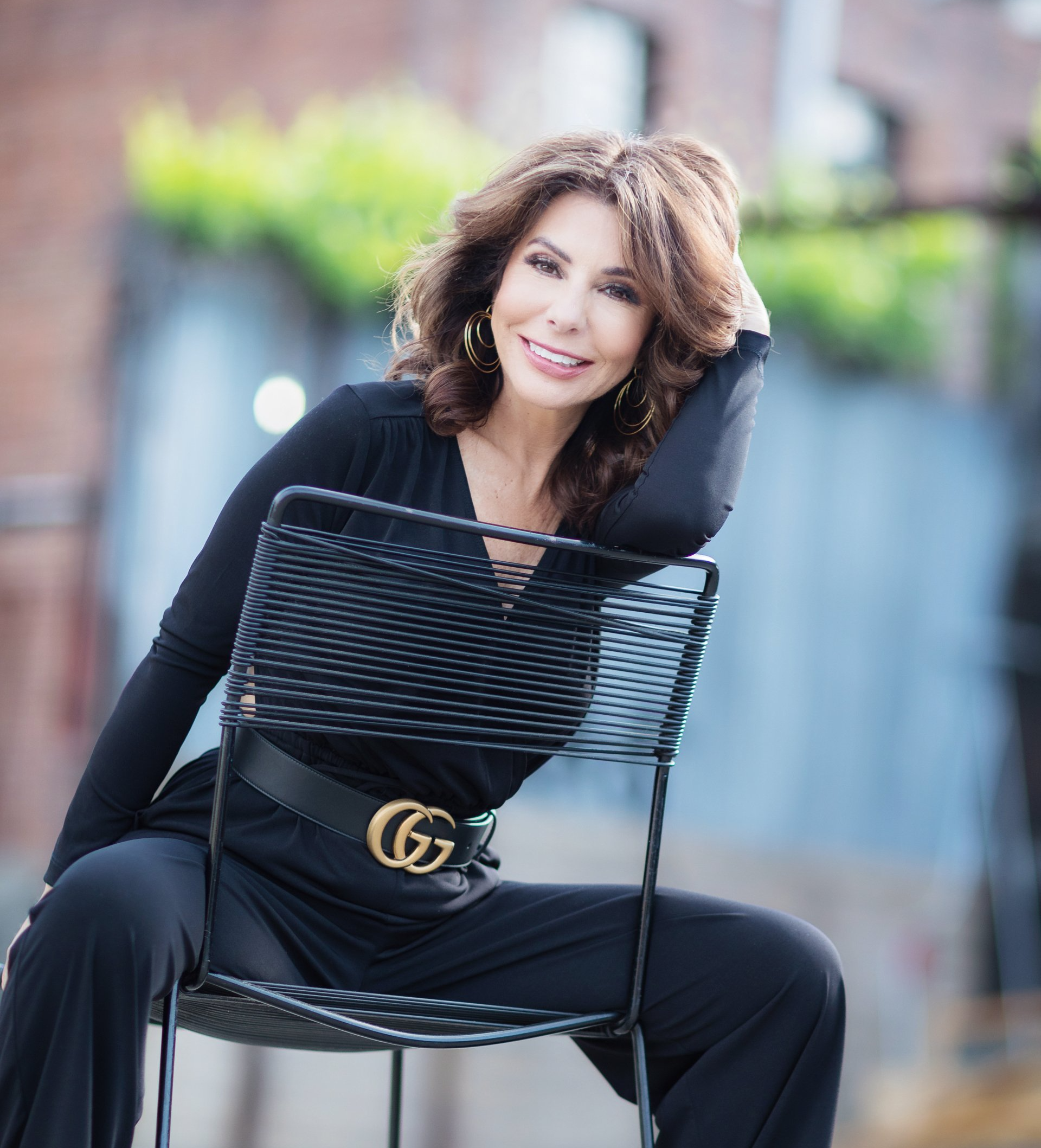 A woman in a black jumpsuit is sitting on a chair