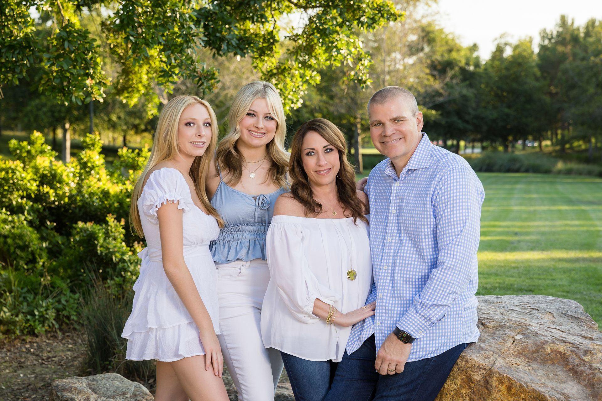 A family is posing for a picture while sitting on a rock in a park.