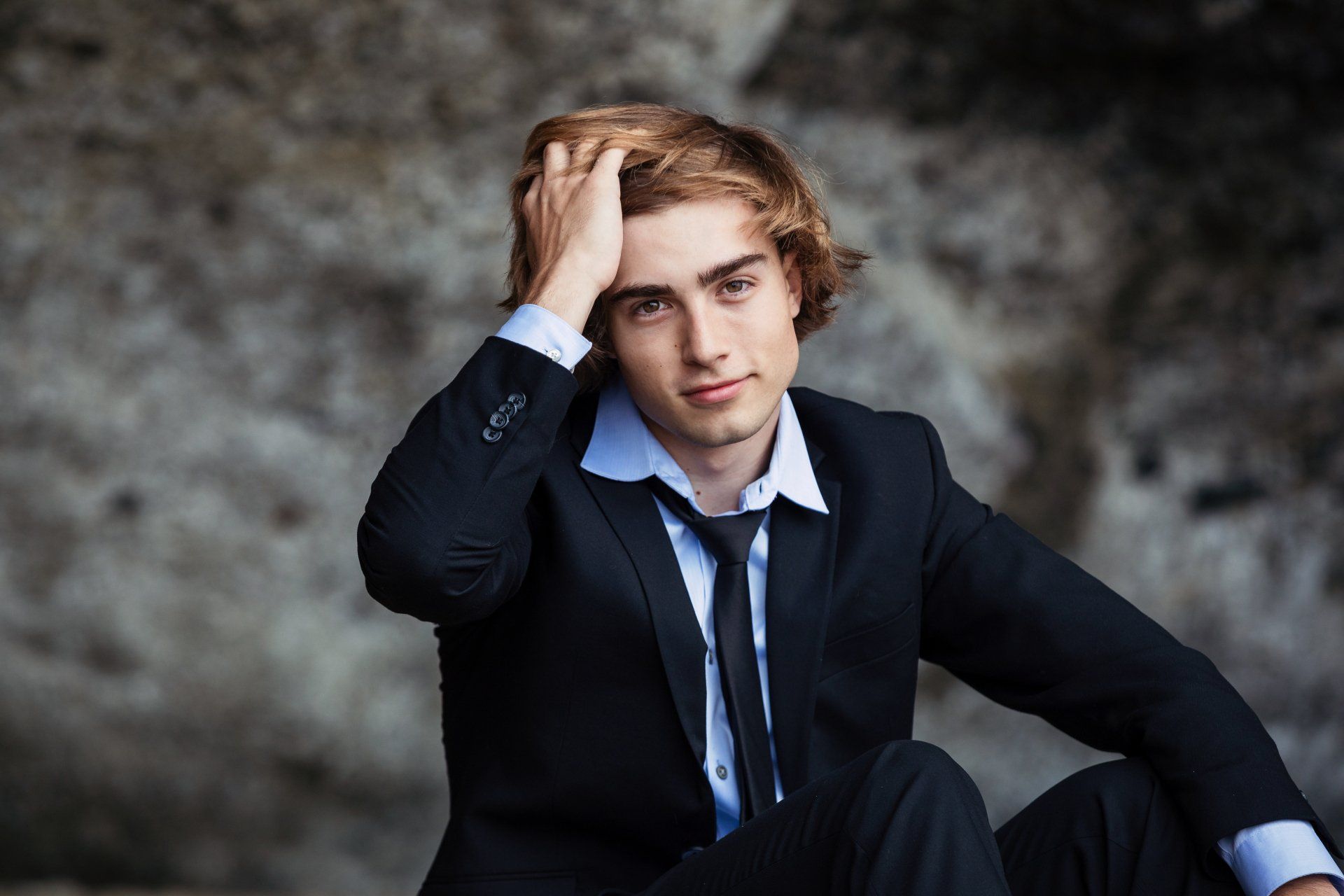 A young man in a suit and tie is sitting on the ground.