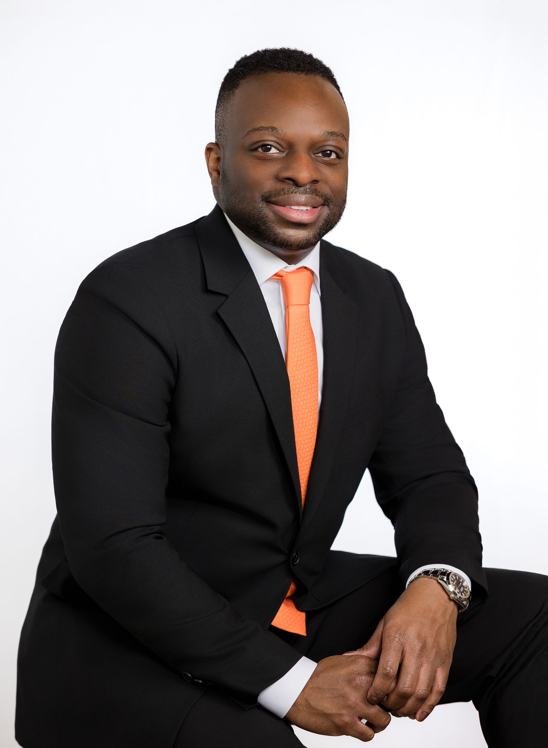 A man in a suit and orange tie is sitting on a chair.