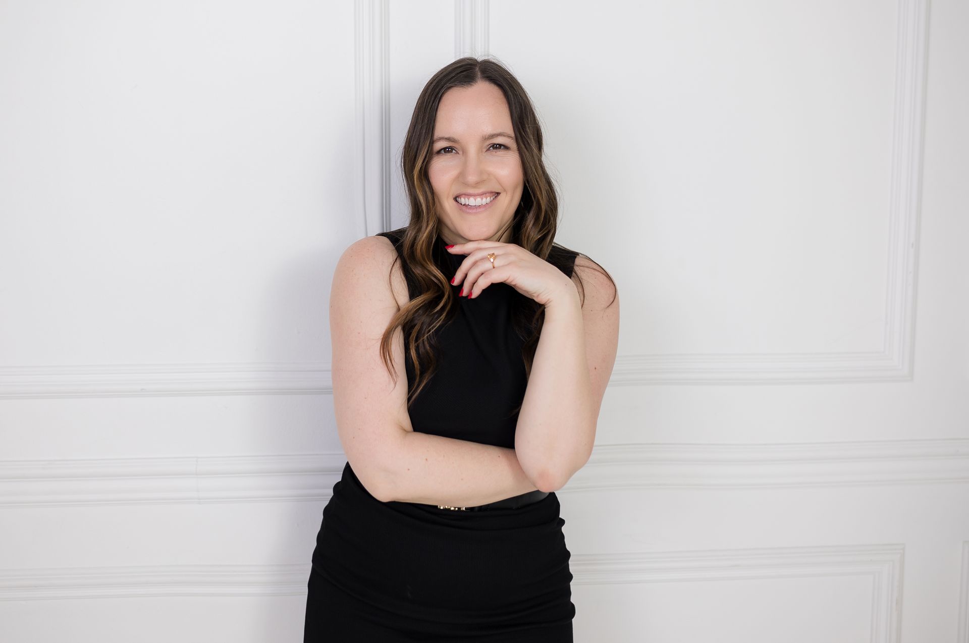 A woman in a black dress is standing in front of a white wall.