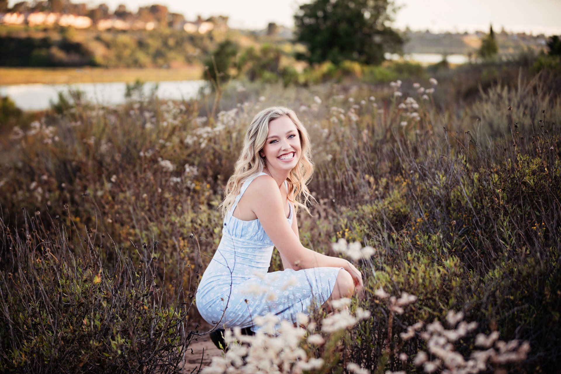 A woman in a blue dress is kneeling in a field of flowers.