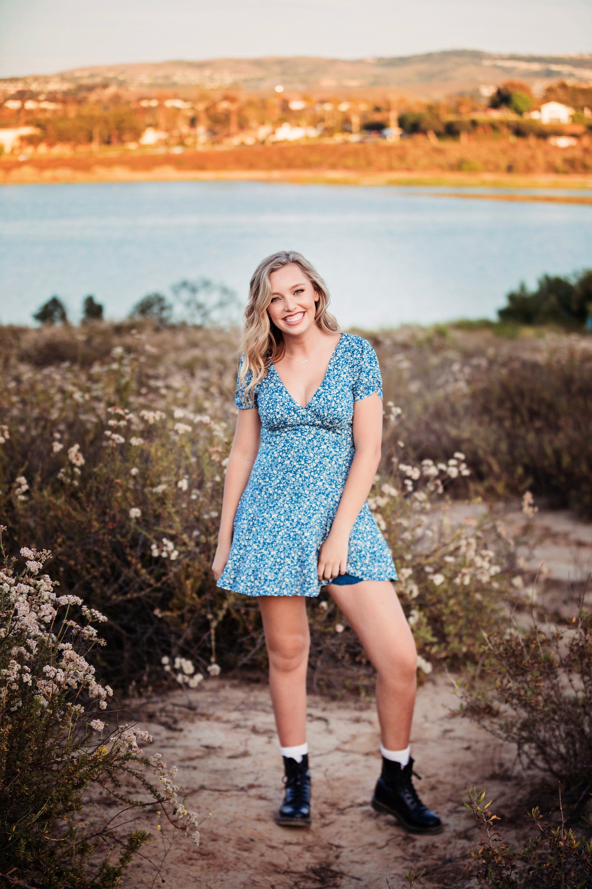 A woman in a blue dress is standing in front of a lake.