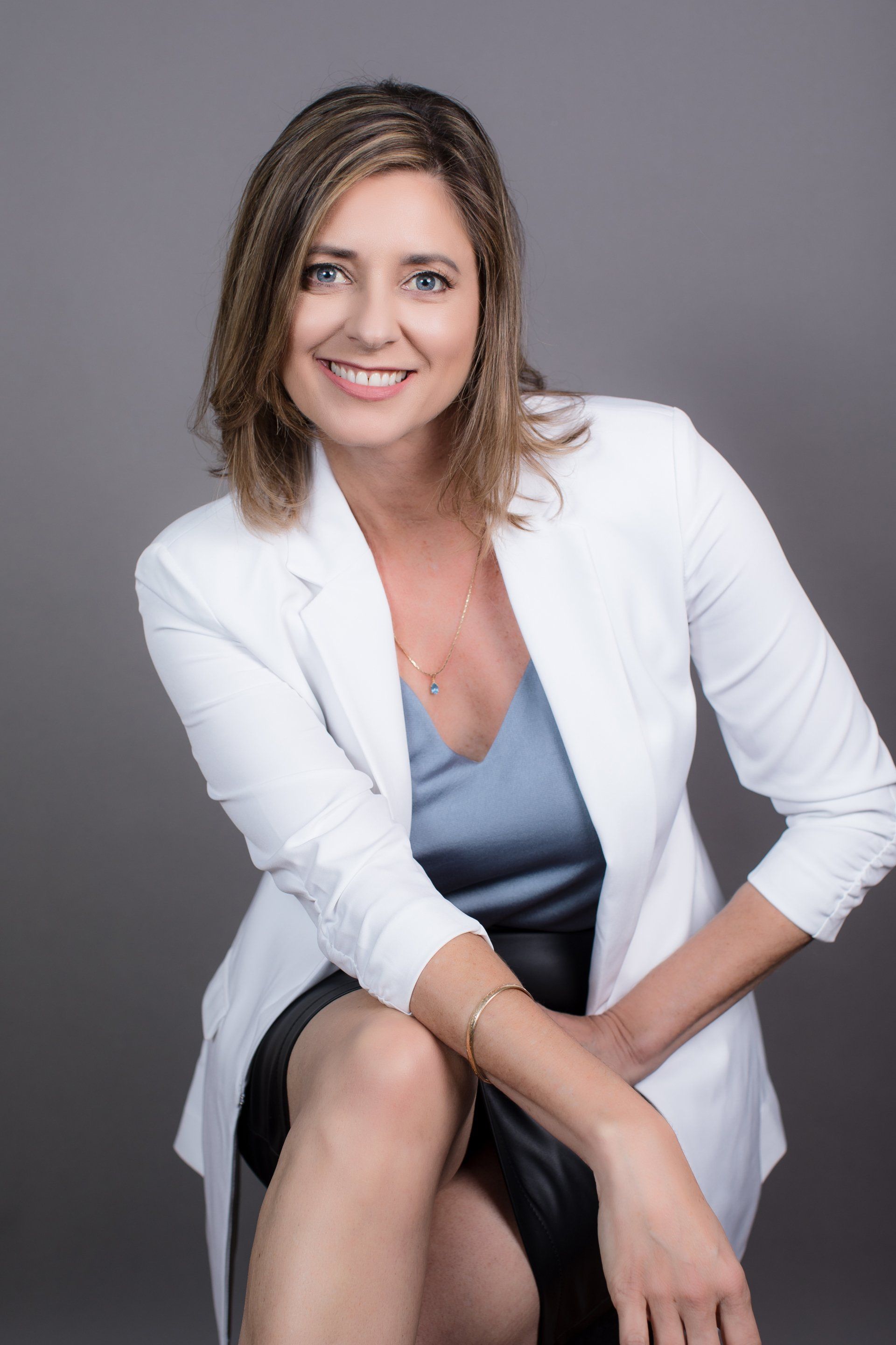 A woman is sitting on a chair with her legs crossed and smiling.