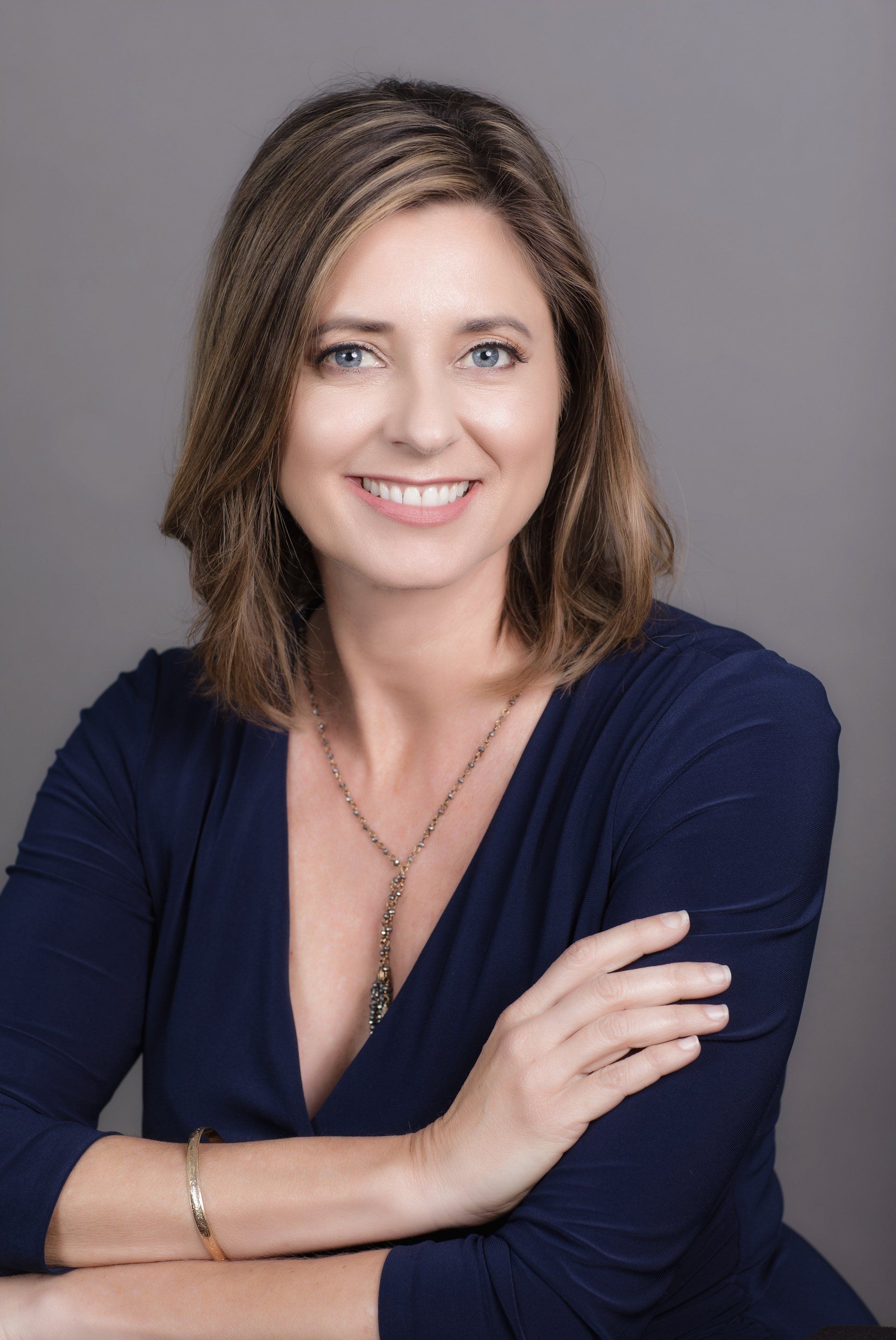 A woman in a blue shirt is smiling with her arms crossed.