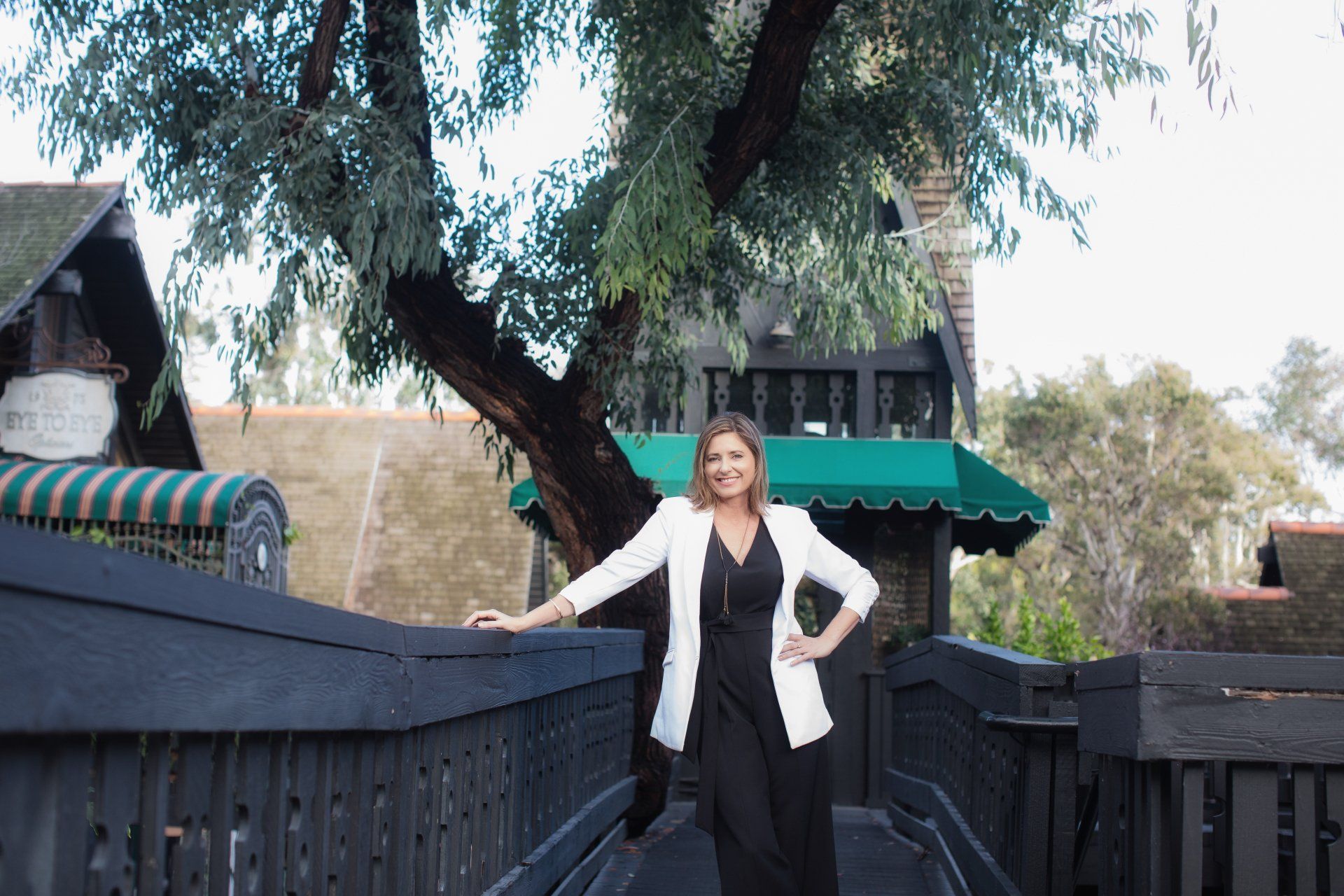 A woman is standing on a bridge in front of a tree.