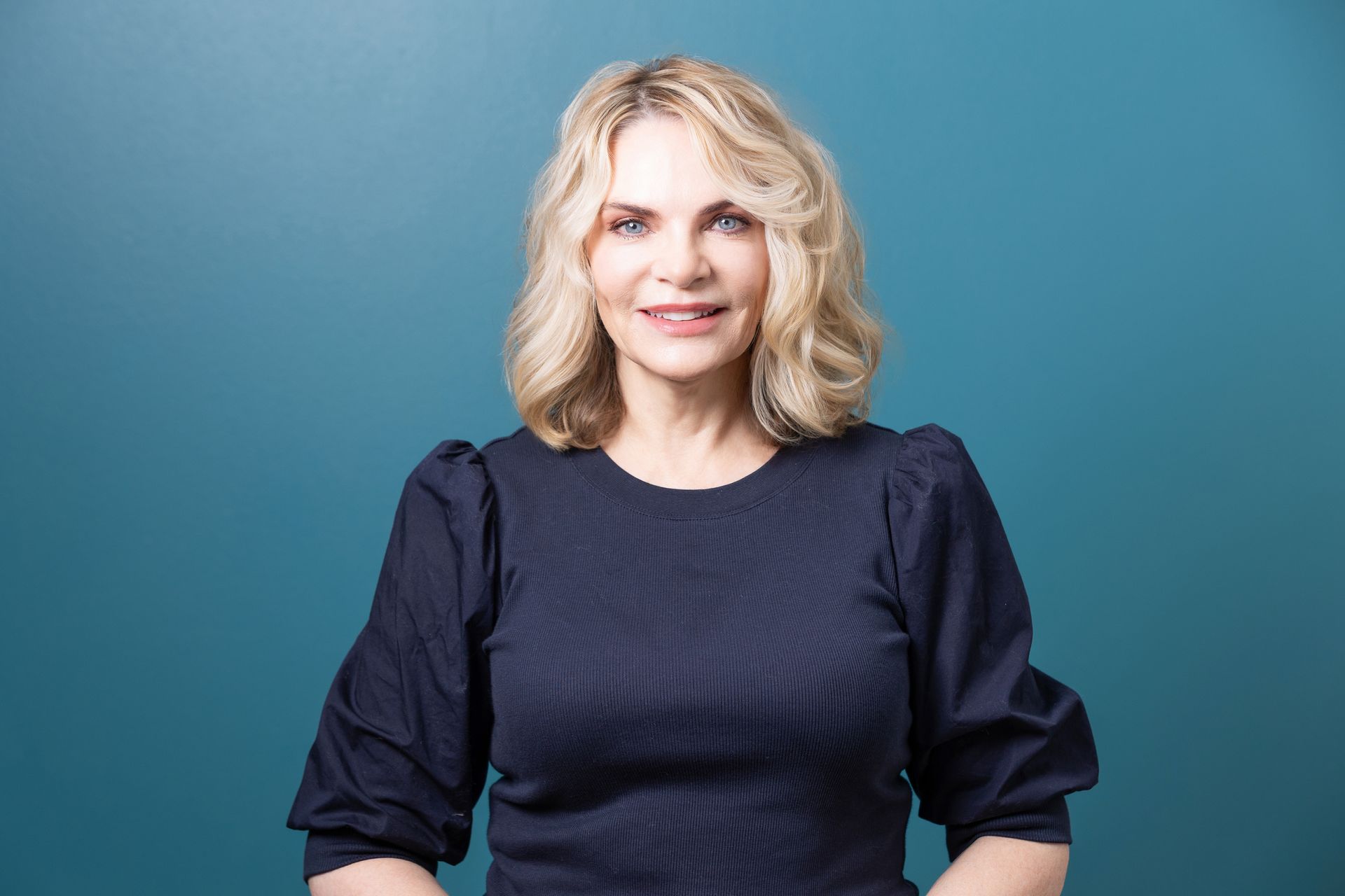 A woman in a blue dress is standing in front of a blue wall.
