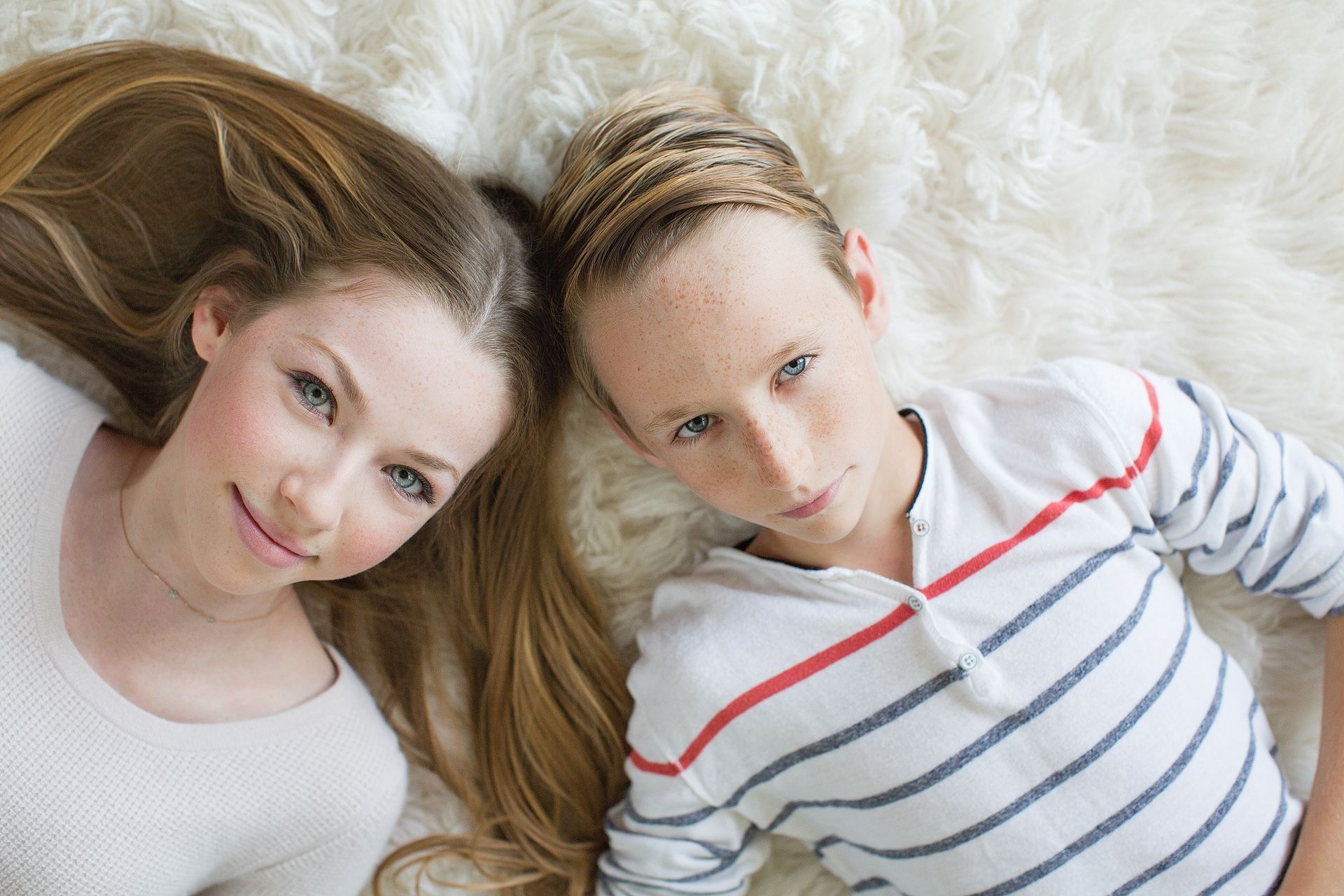 Siblings laying on the carpet in front of the fireplace looking up at the camera in their Orange County home.