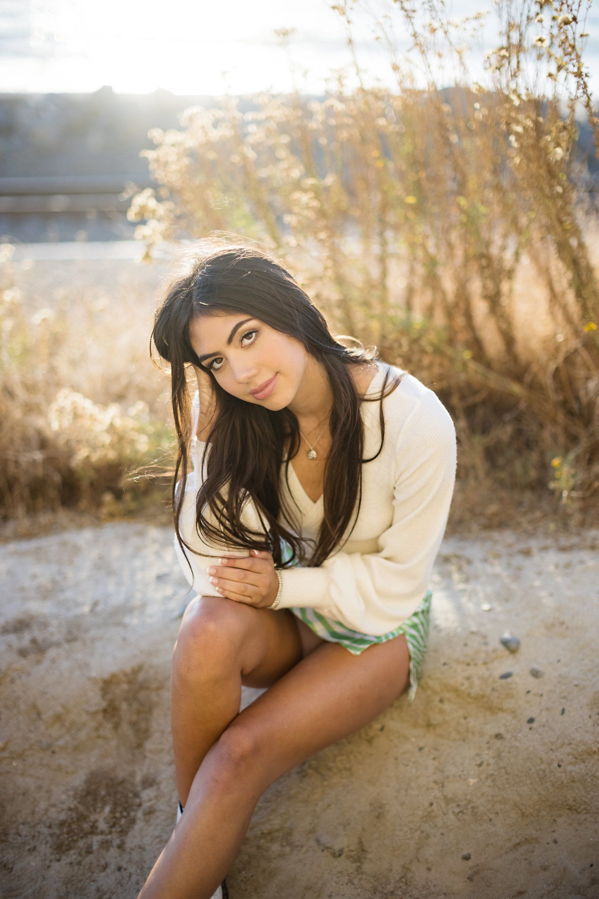 A woman in a white sweater and shorts is sitting on a rock.