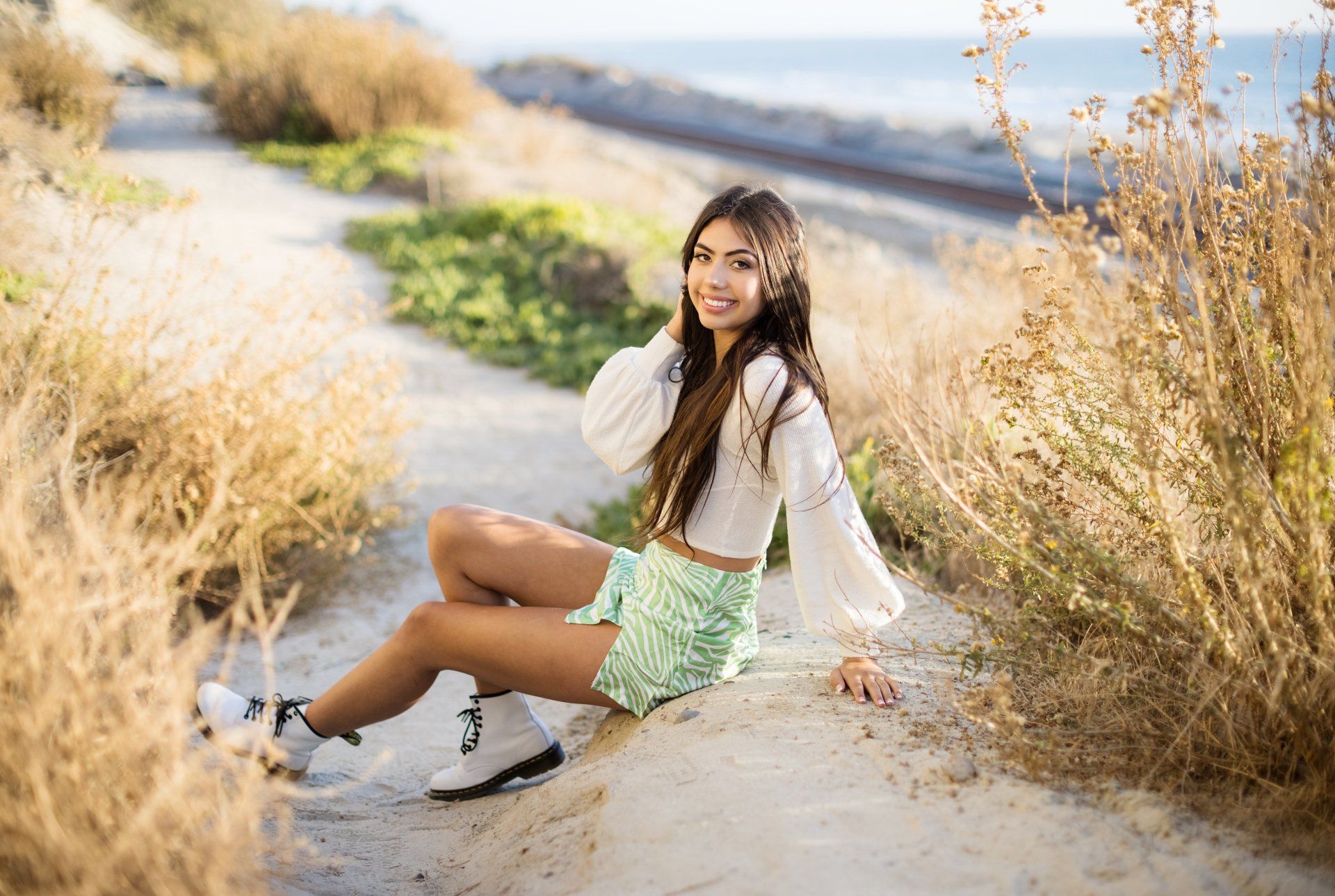 A young woman is sitting on the side of a dirt road.