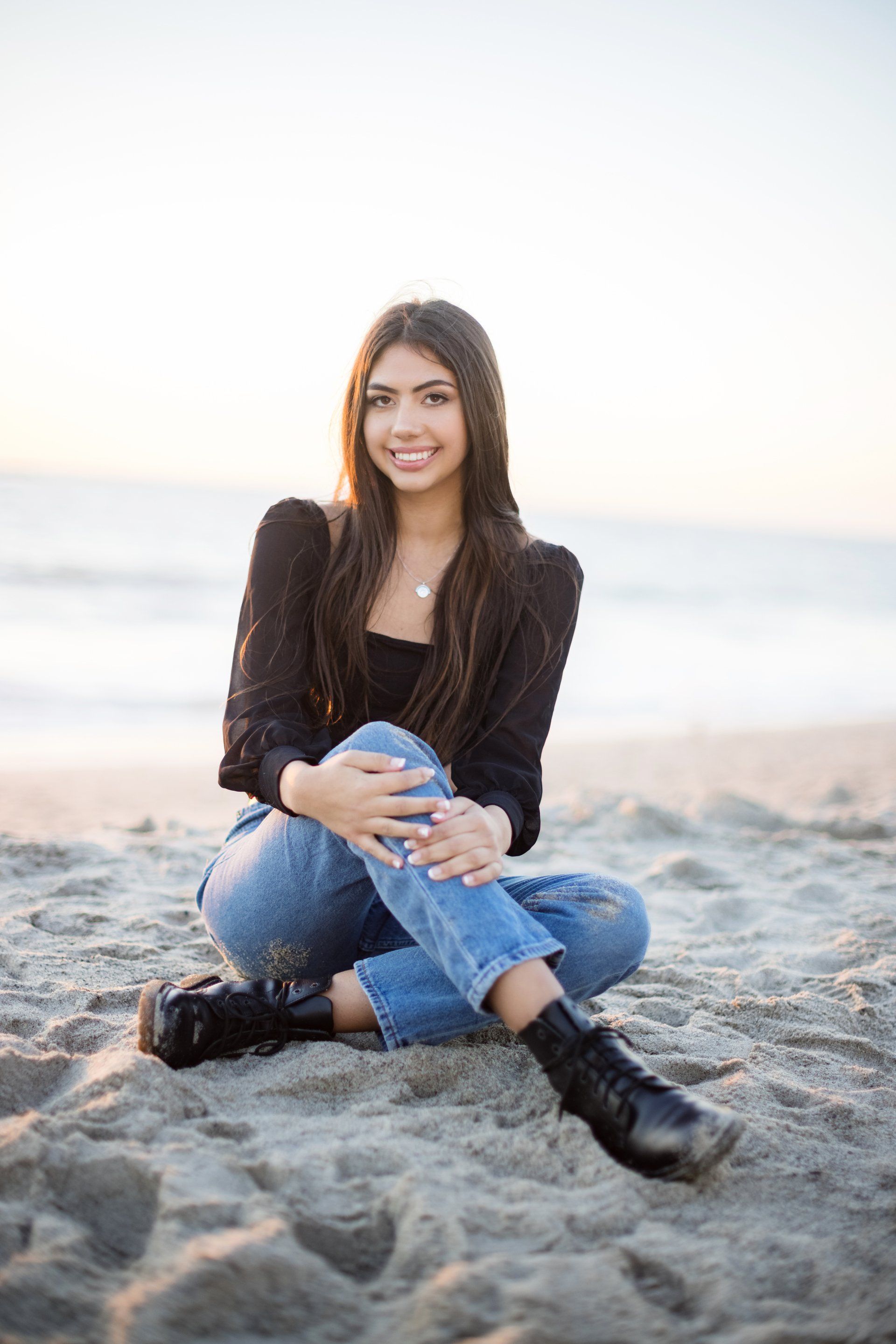 A young woman is sitting on the beach with her legs crossed.