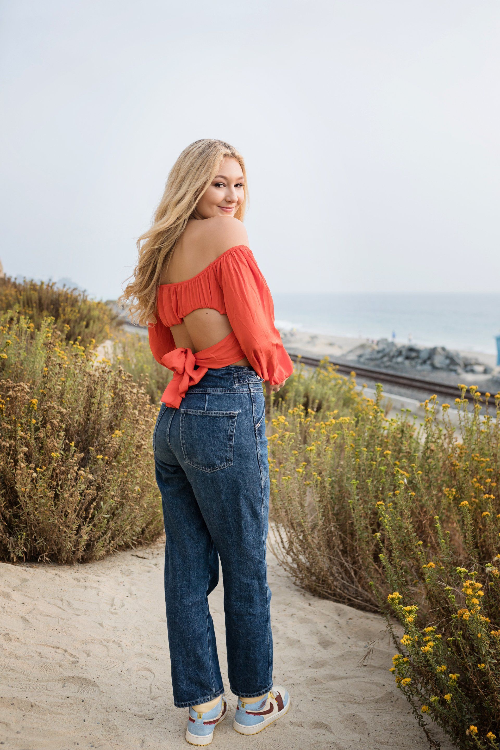 The woman is wearing a red off the shoulder top and blue jeans.