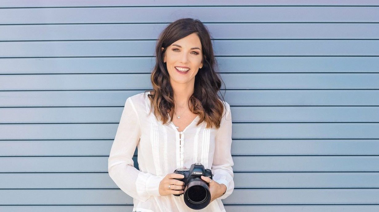 A woman is holding a camera in front of a blue wall.