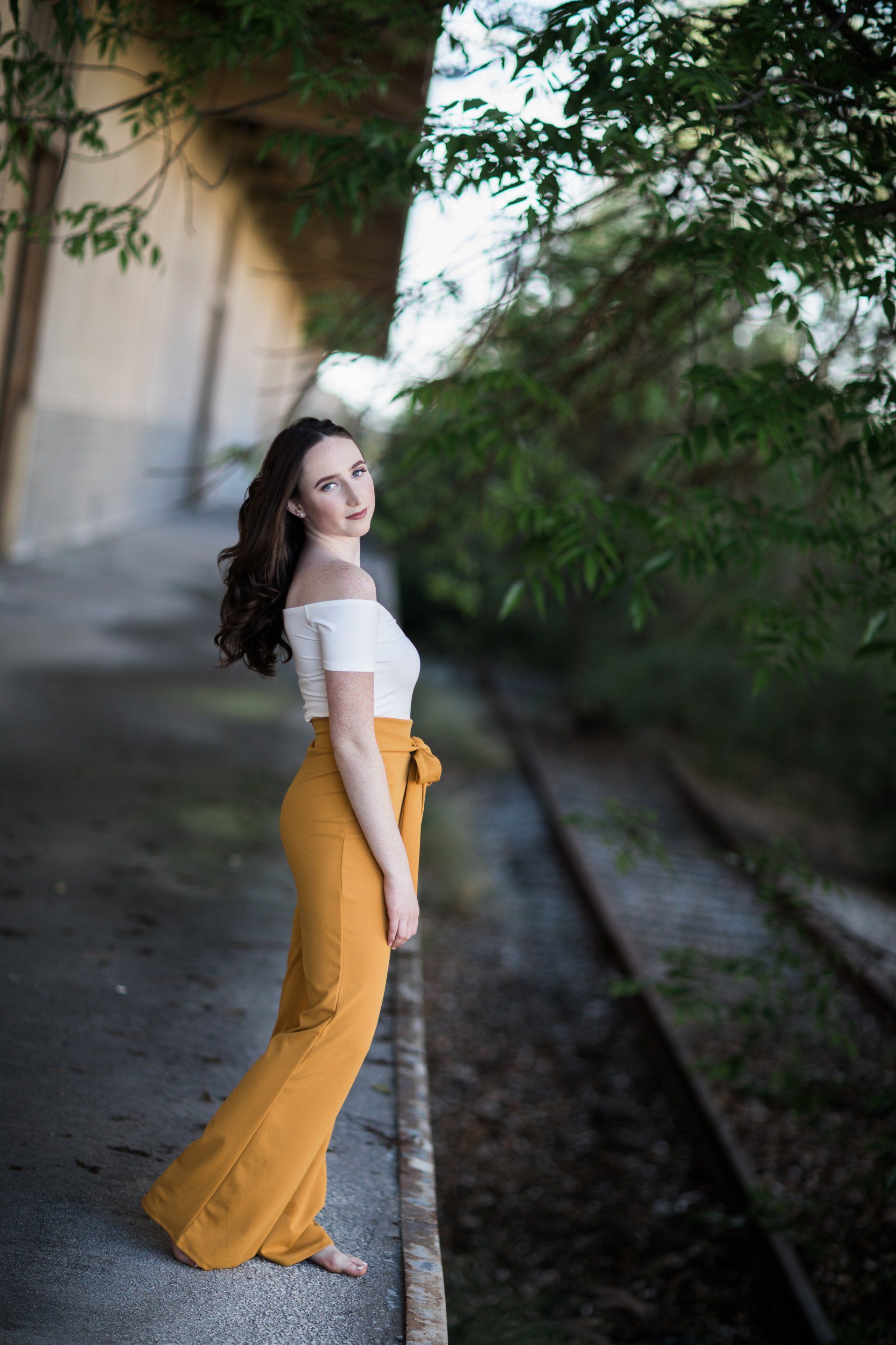 A woman in yellow pants and a white top is standing on train tracks.