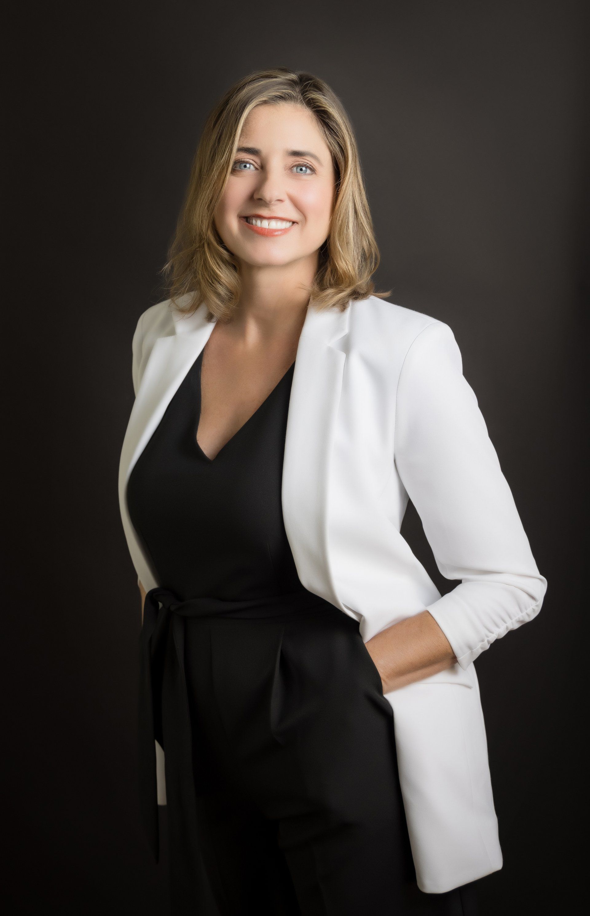 A woman in a black dress and white jacket is smiling for the camera.