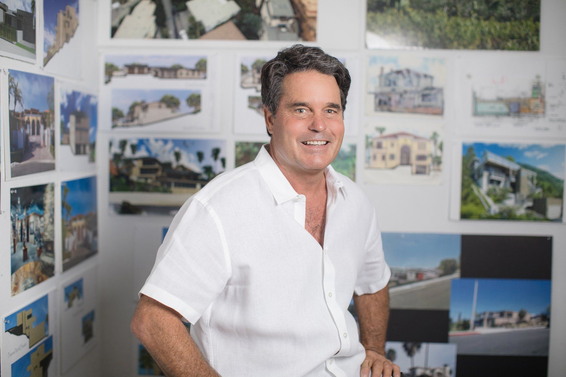 A man in a white shirt is standing in front of a wall of pictures.