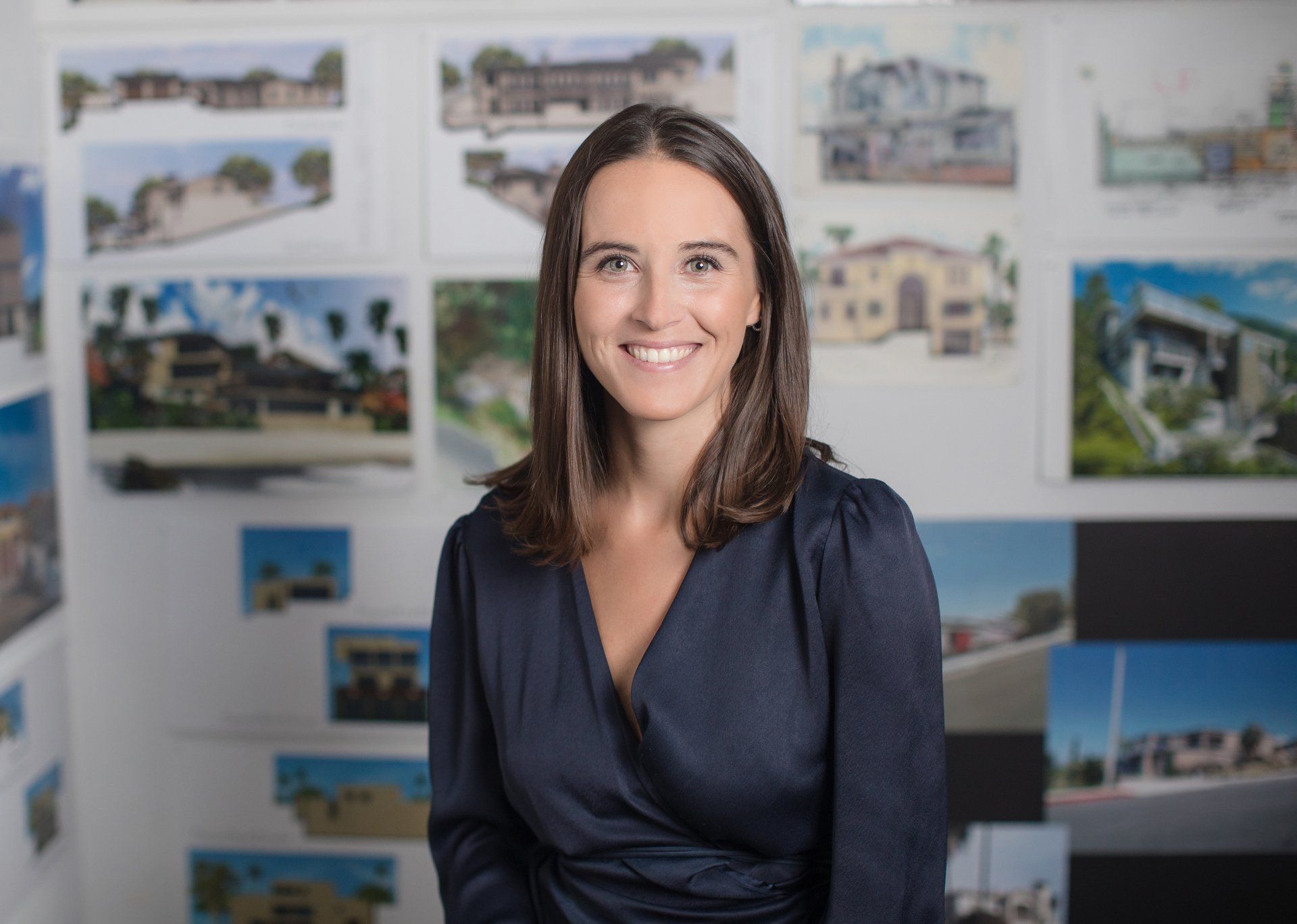 A woman in a blue dress is smiling in front of a wall of drawings.