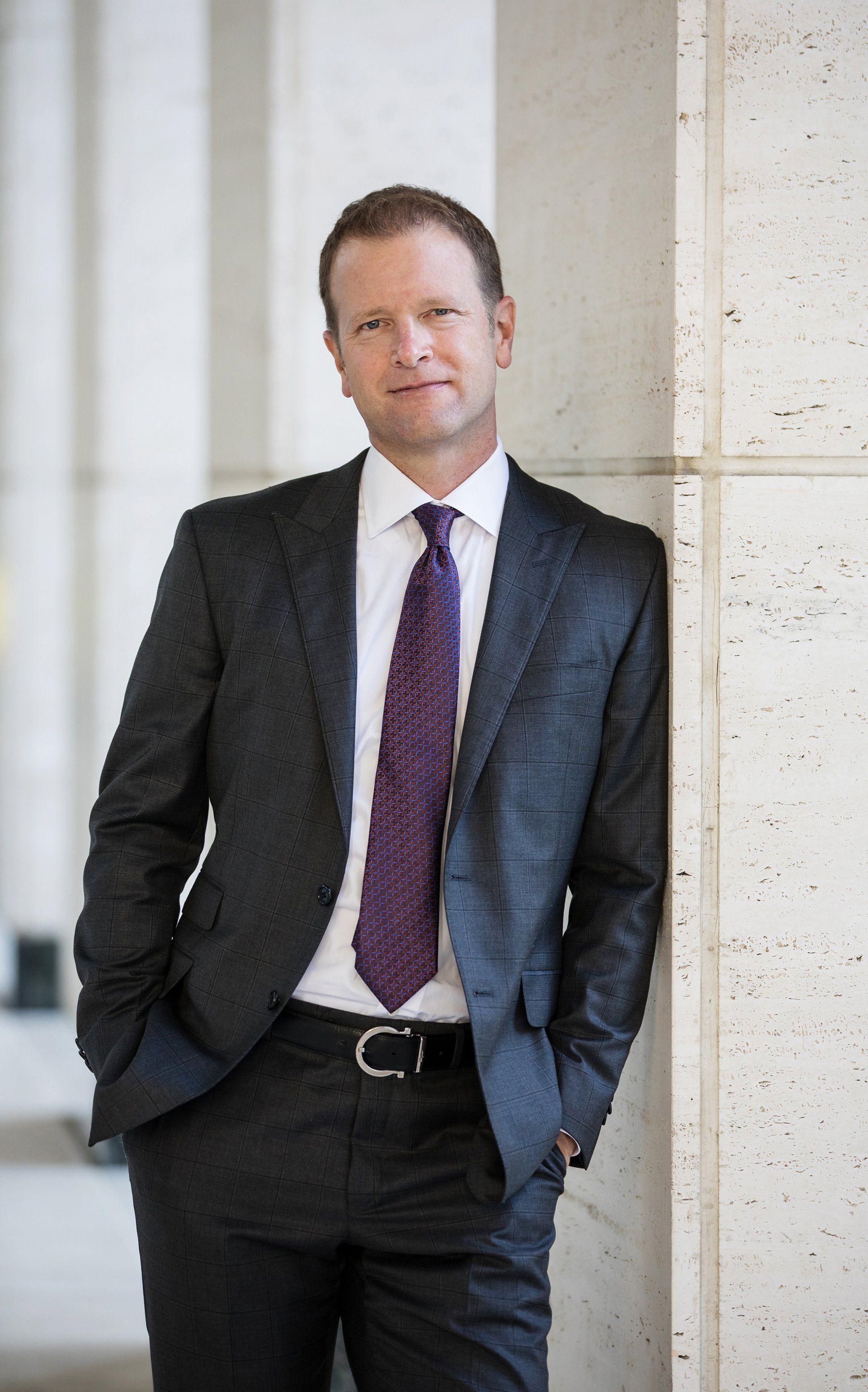 A man in a suit and tie is leaning against a wall.