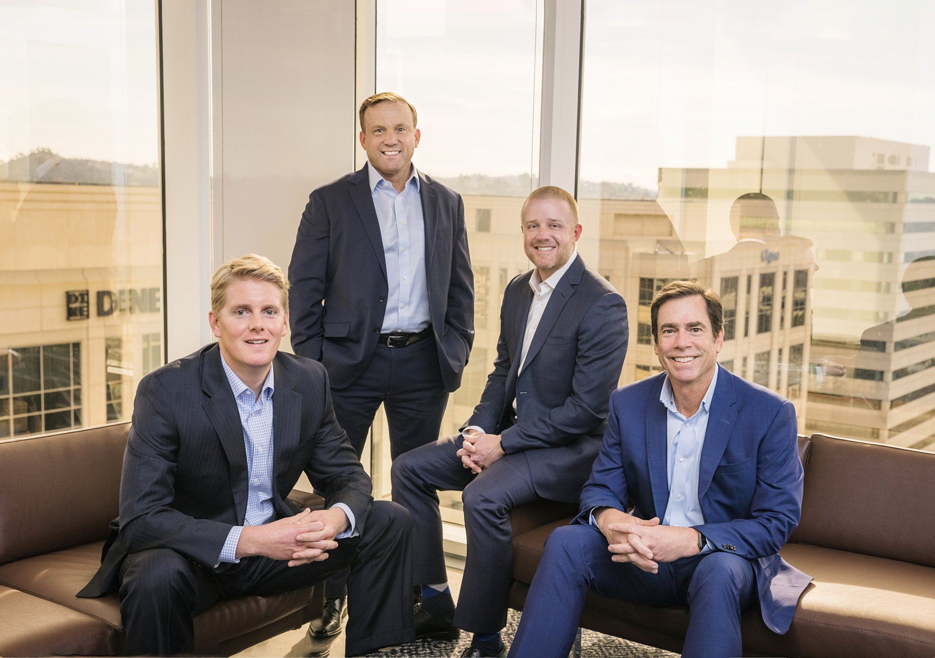 A group of men in suits are sitting on a couch in front of a window.